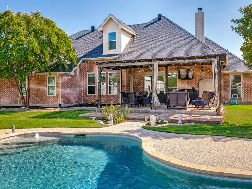 Brick exterior with a dormer window, covered patio with a pergola, and a private swimming pool with a water feature