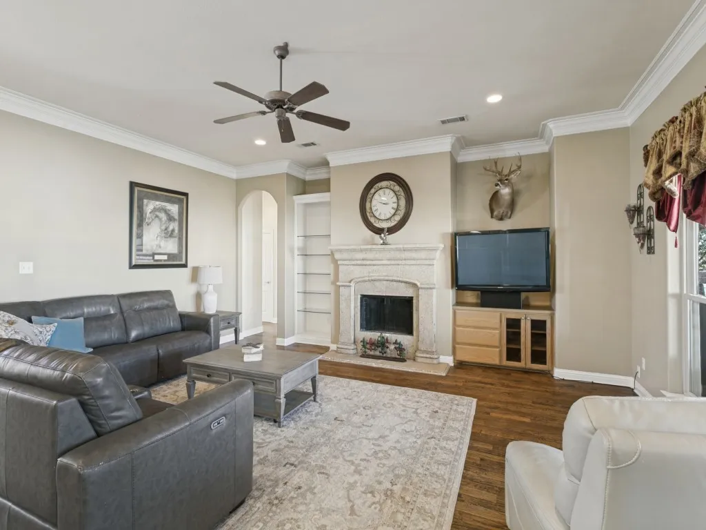 Elegant living room showcasing a fireplace with white surround and mantel, hardwood flooring, crown molding, recessed lighting, and a ceiling fan