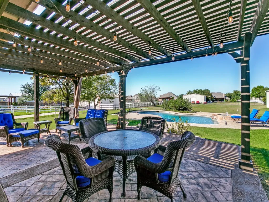 Expansive outdoor living area featuring a covered patio with string lighting, stamped concrete flooring, a fenced backyard, and a built-in swimming pool
