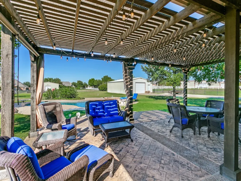 Expansive outdoor living area featuring a wooden pergola, string lighting, patterned concrete patio, and a swimming pool