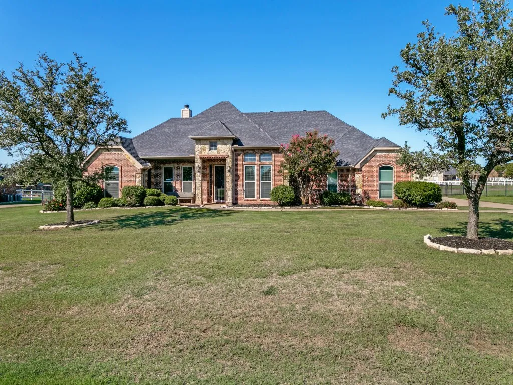 Brick exterior with stone accents, a dark shingle roof, and mature landscaping