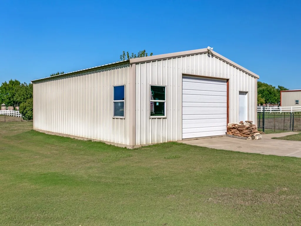 Metal-sided structure with a pitched roof, two windows, a white roll-up garage door, and a single entry door