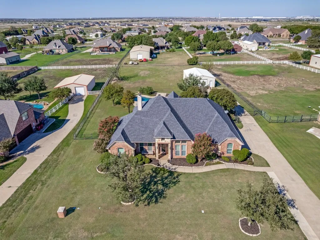 Brick residence with a dark shingle roof, extensive concrete driveway, and mature landscaping