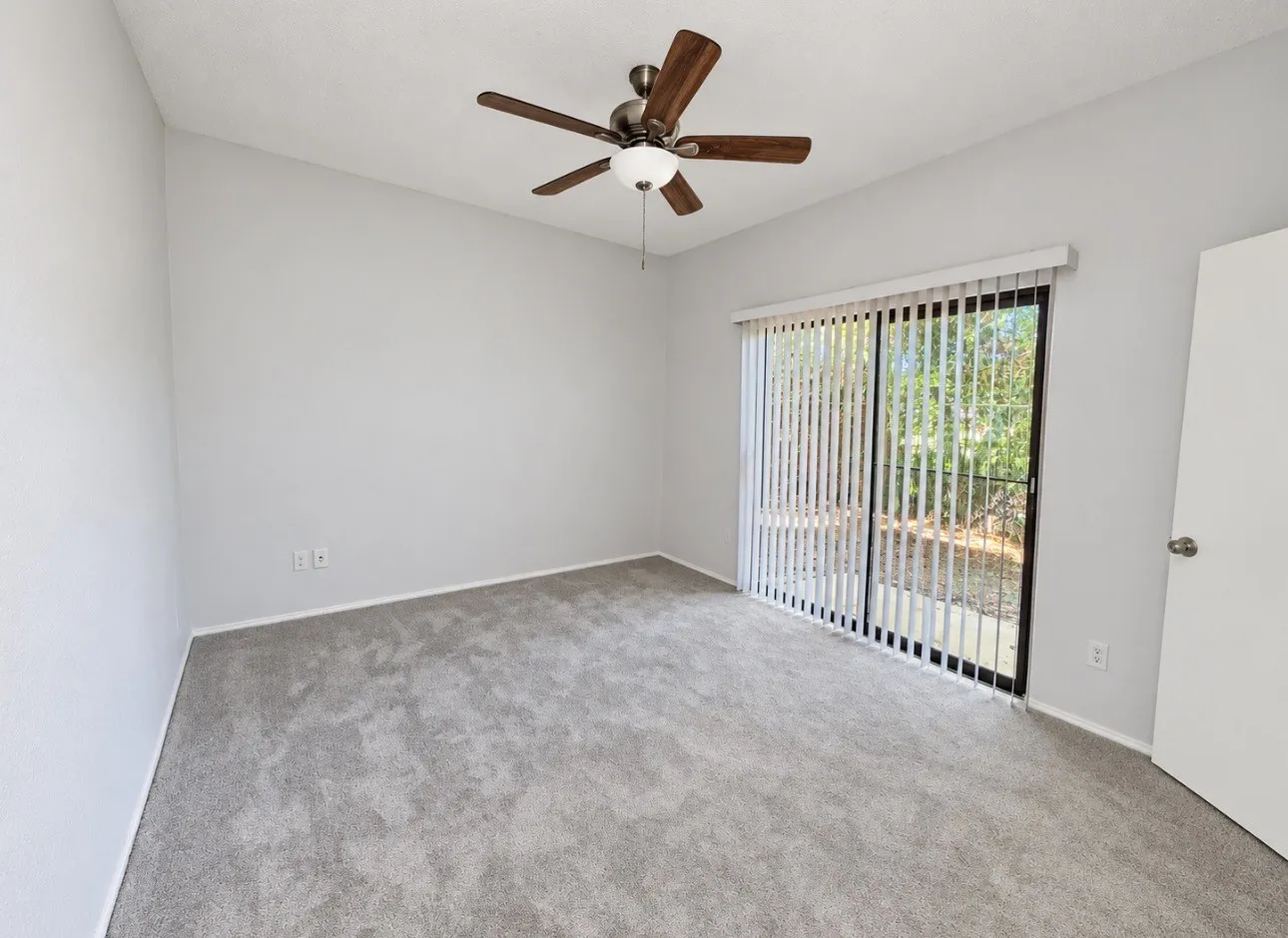 Sliding glass door with vertical blinds, ceiling fan with integrated lighting, and neutral tone carpeting