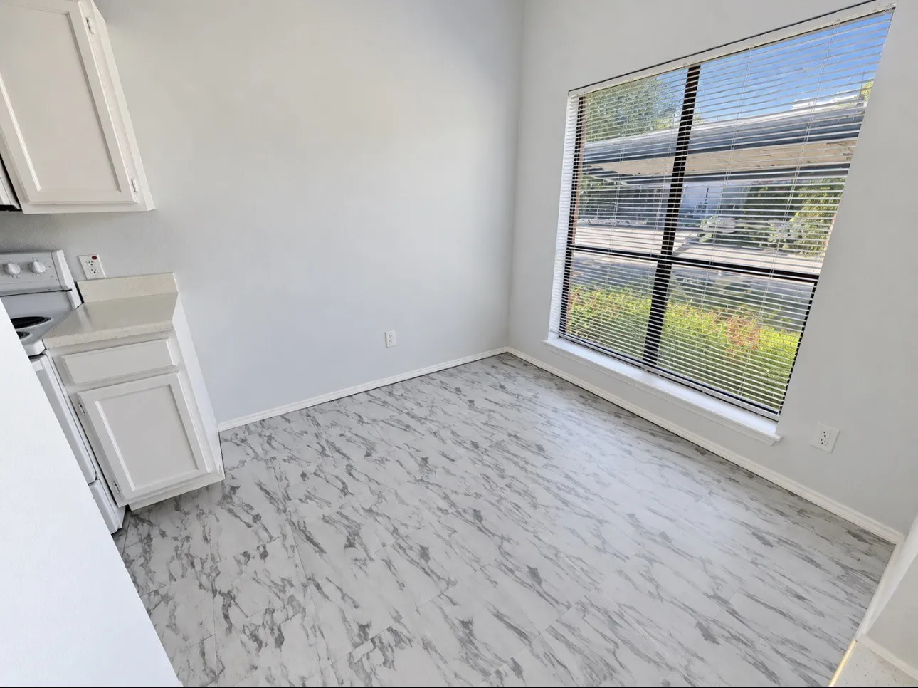 White cabinetry with a light-toned countertop, a window with horizontal blinds, and patterned flooring