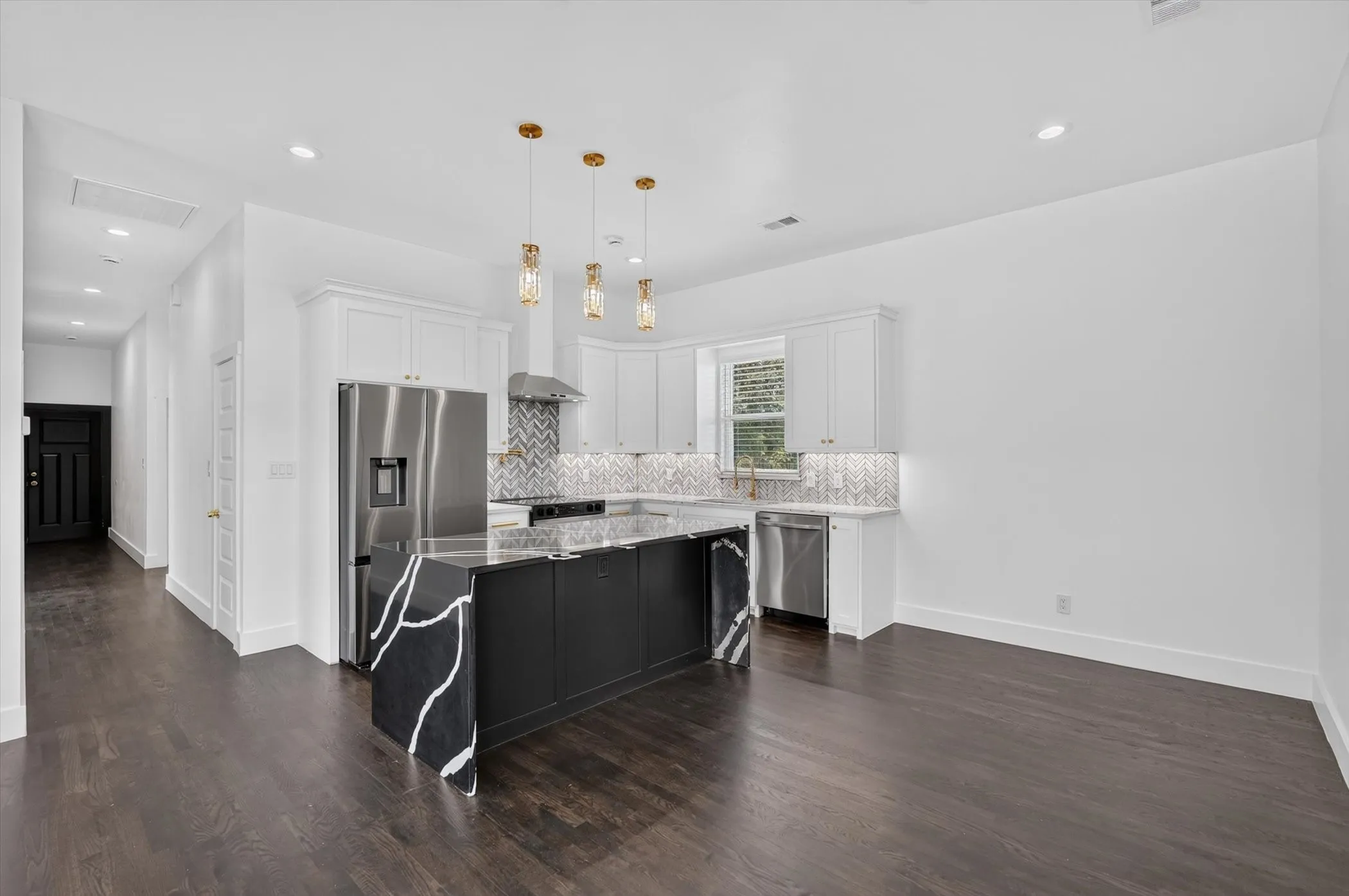 Kitchen featuring a central island with black cabinetry and a light-veined dark countertop, white upper and lower cabinetry, stainless steel appliances, and a chevron pattern tile backsplash