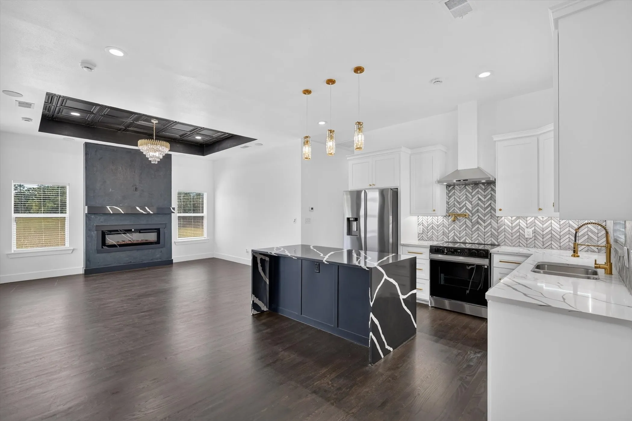 Open-concept living space featuring wood-finish flooring, a contemporary fireplace, and a kitchen island with a waterfall countertop