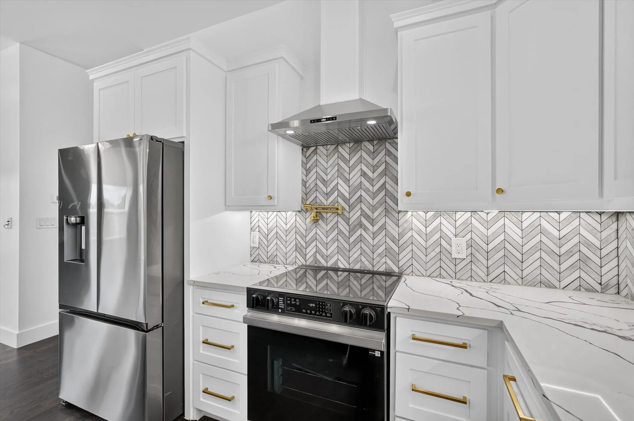 White shaker cabinetry with gold-tone hardware, stainless steel appliances, herringbone tile backsplash, and stone-finish countertops