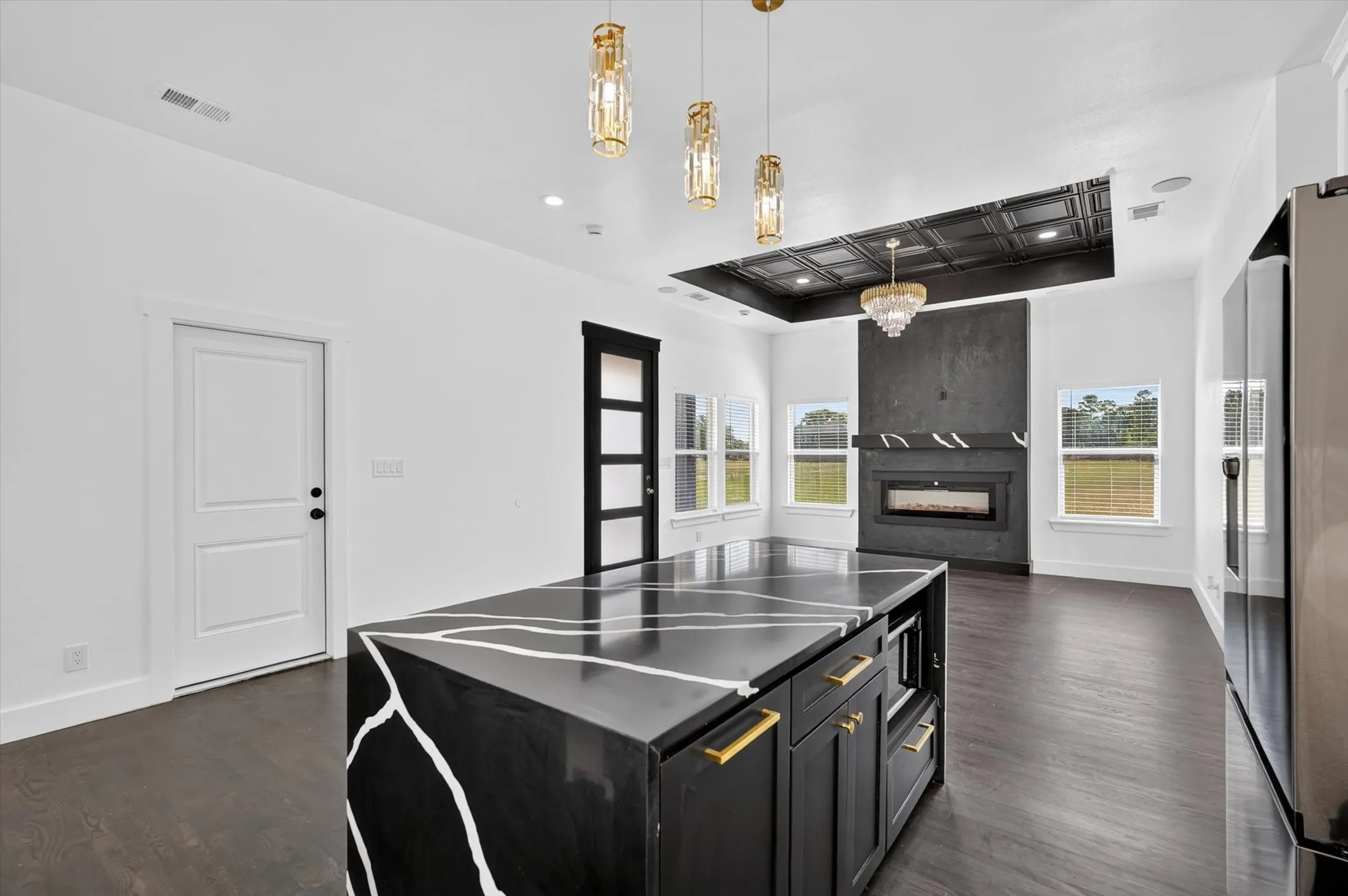 Spacious open-concept interior featuring wood-finish flooring, a custom island with a unique countertop, a fireplace with a textured surround, and recessed ceiling details with integrated lighting