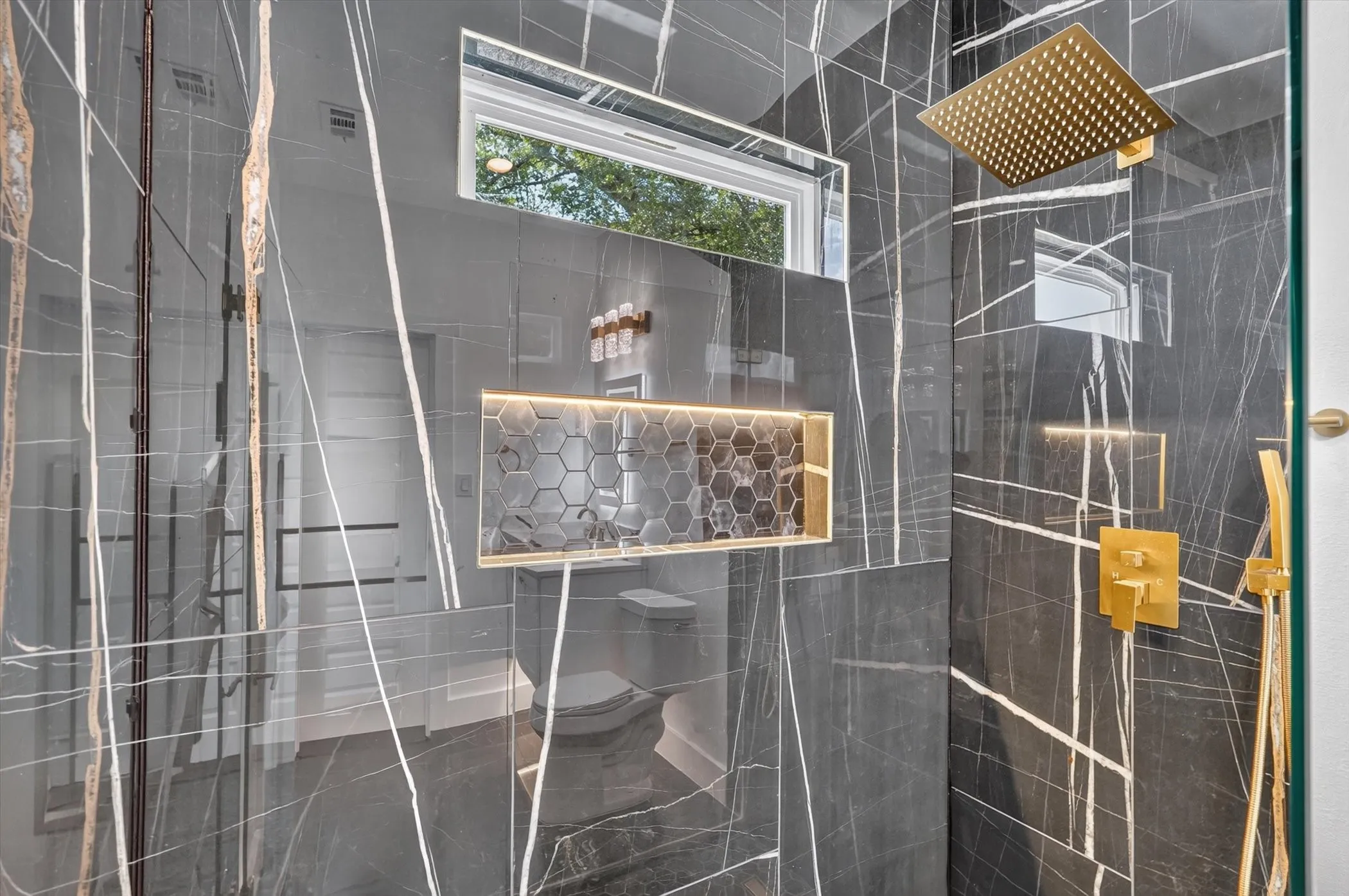 Shower with large format stone-finish wall tiling, gold-finish fixtures, and a recessed niche with honeycomb tile