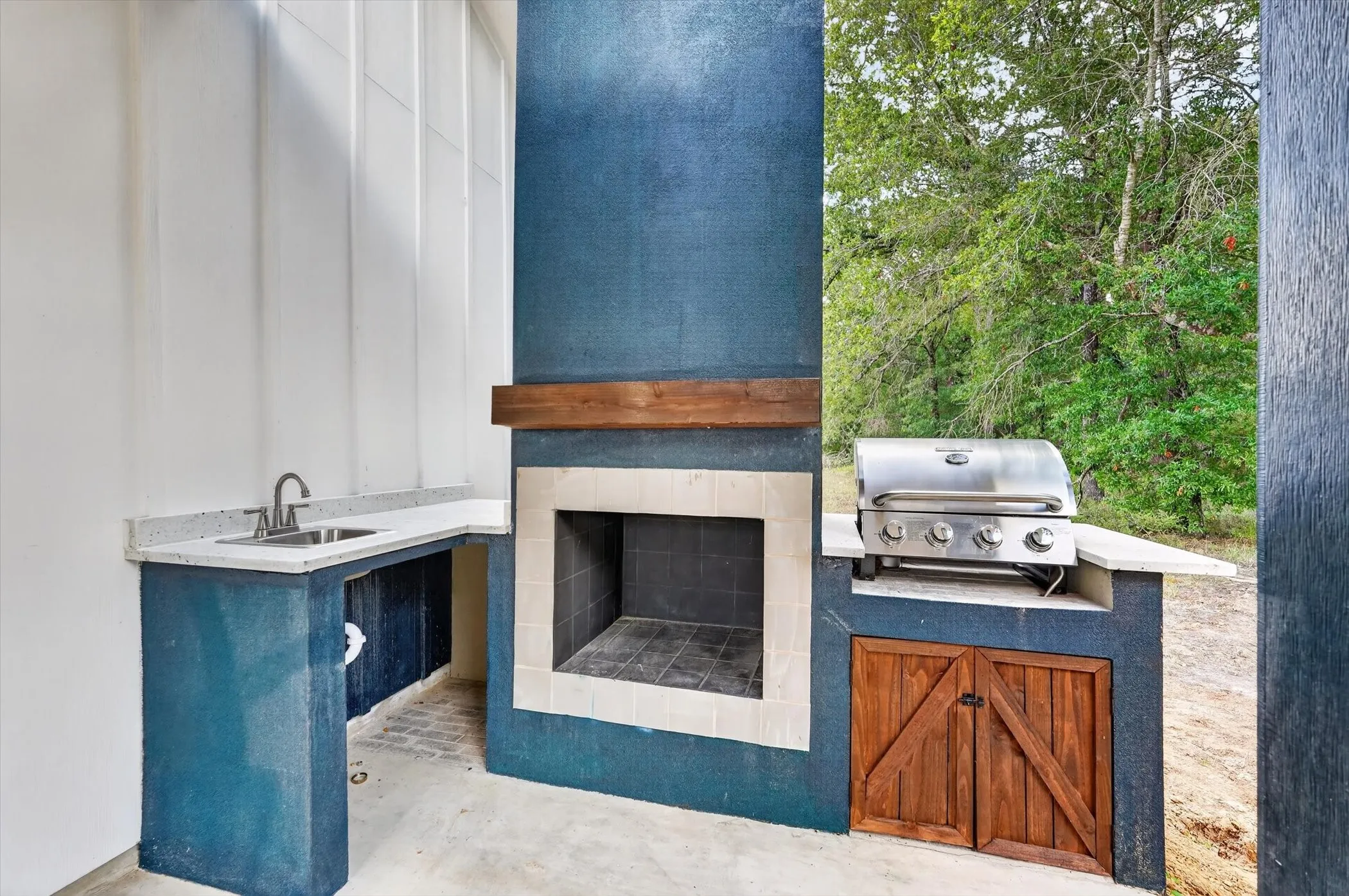 Outdoor kitchen featuring a built-in grill, integrated sink, and wood-front storage cabinetry