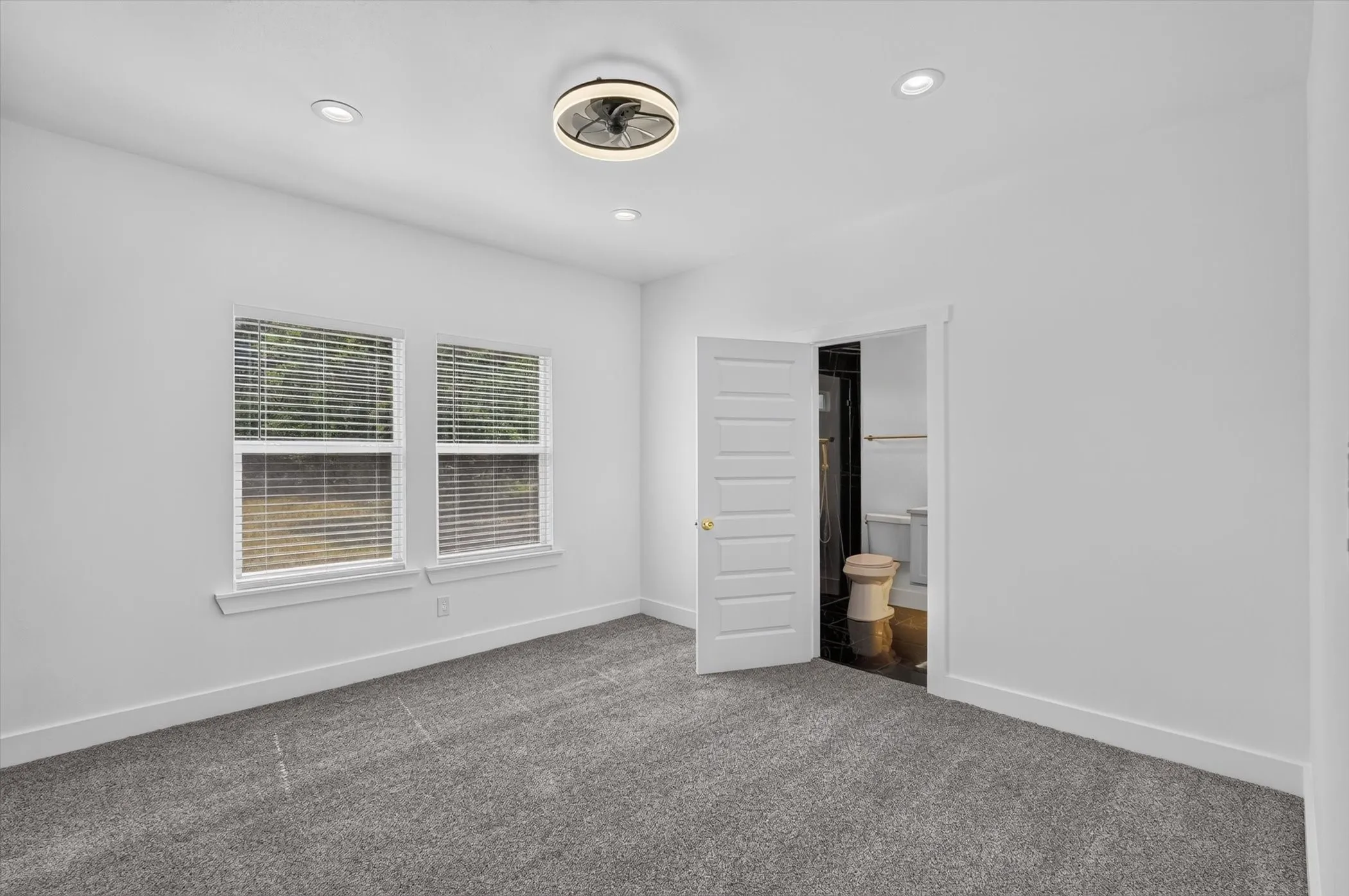 Recessed lighting, ceiling fan with integrated light, dual windows with blinds, plush gray carpeting, and white paneled door