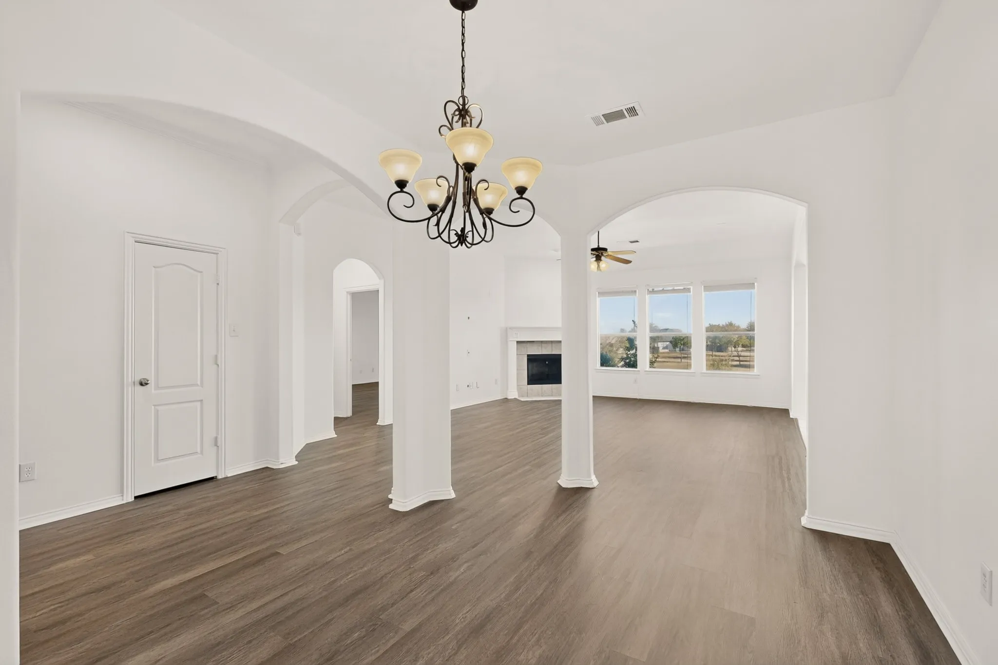 Open-concept living area featuring wood-finish flooring, arched doorways, a chandelier, and ample natural light from multiple windows