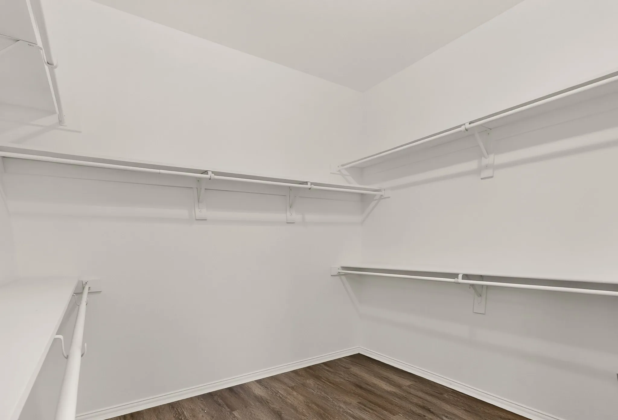 White built-in shelving, white clothes rods, and wood-finish flooring