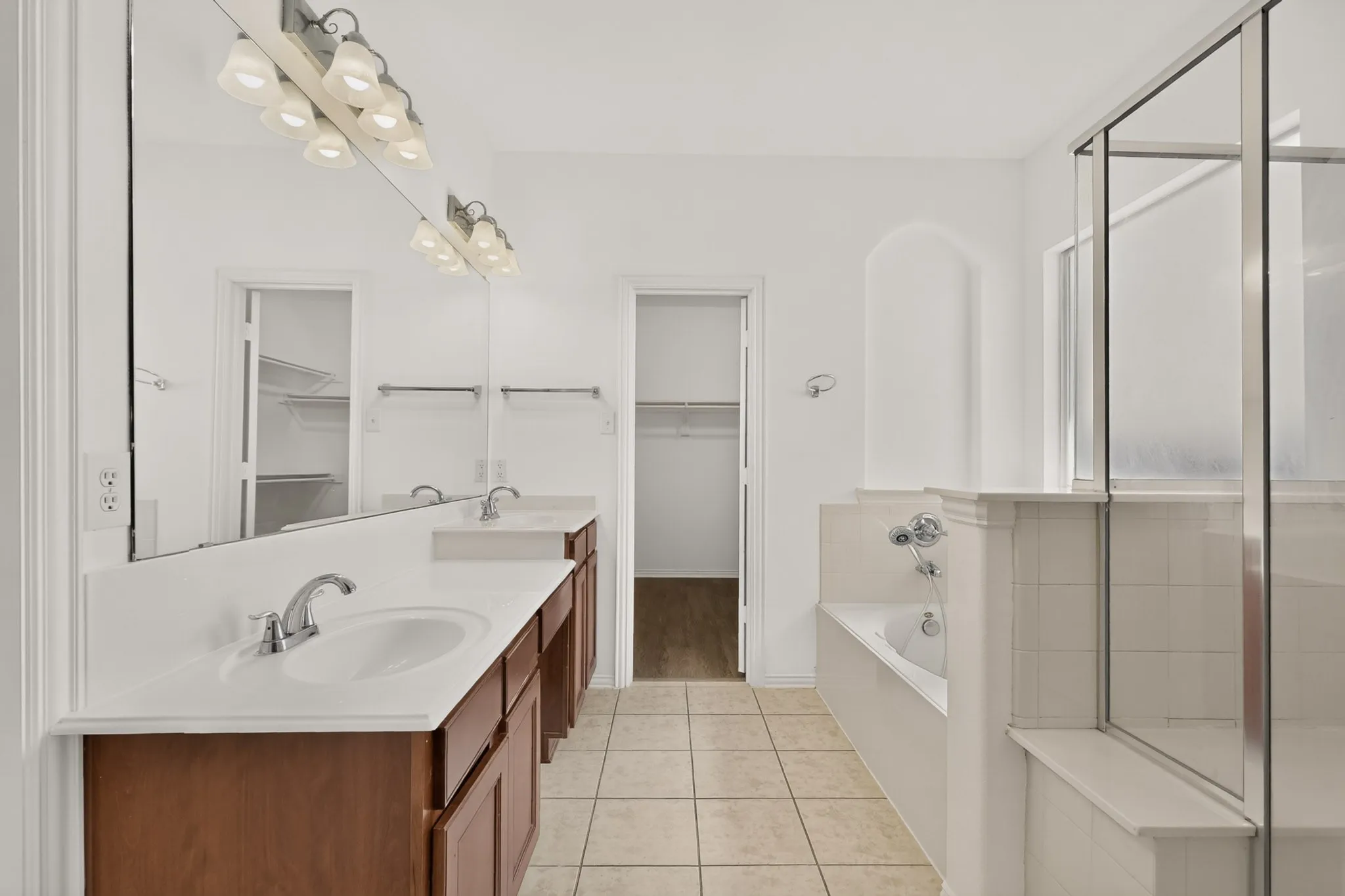 Dual vanity with integrated sinks, a built-in tub, a glass-enclosed shower, and tile flooring
