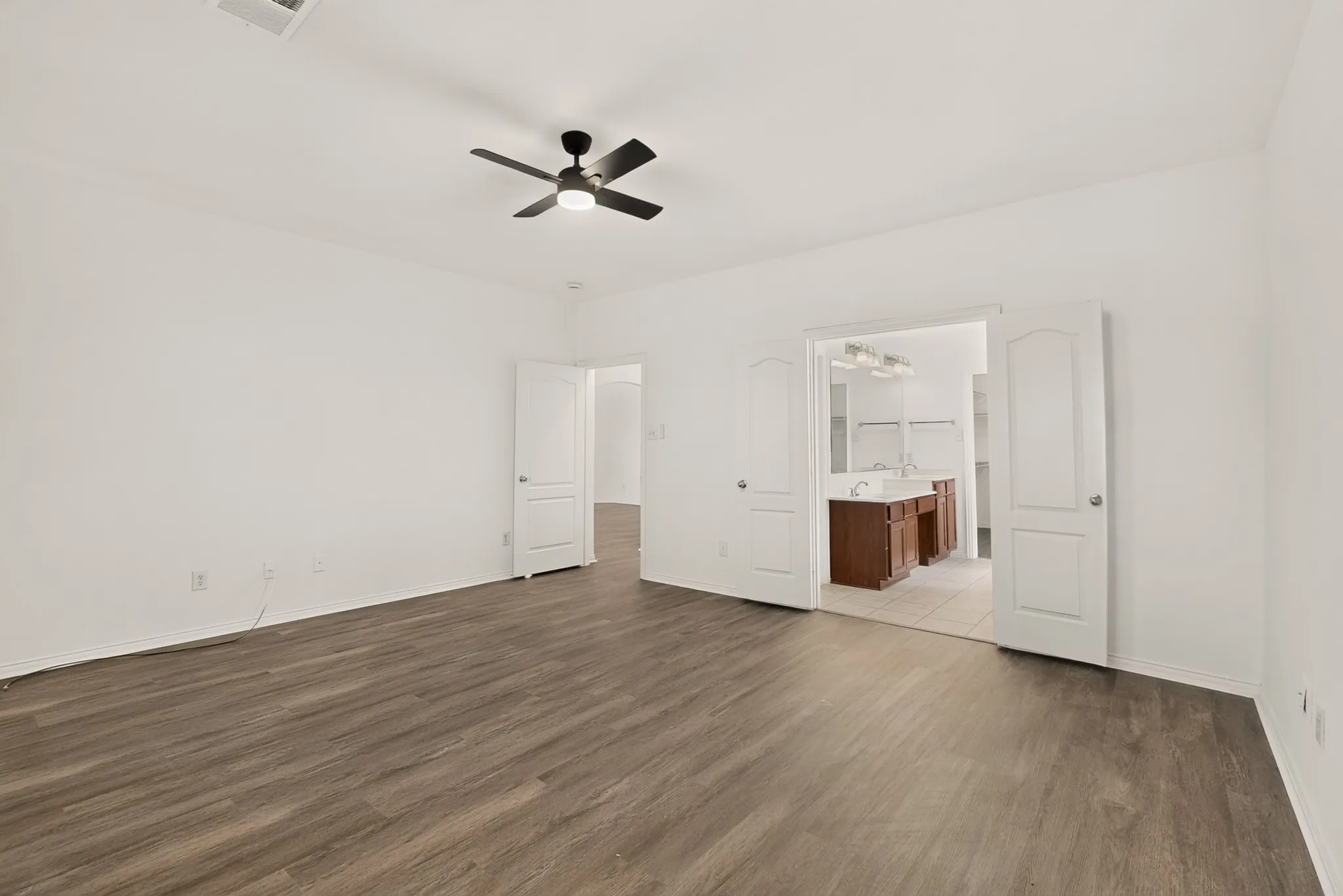 Spacious room featuring wood-finish flooring, a ceiling fan with integrated lighting, and white walls