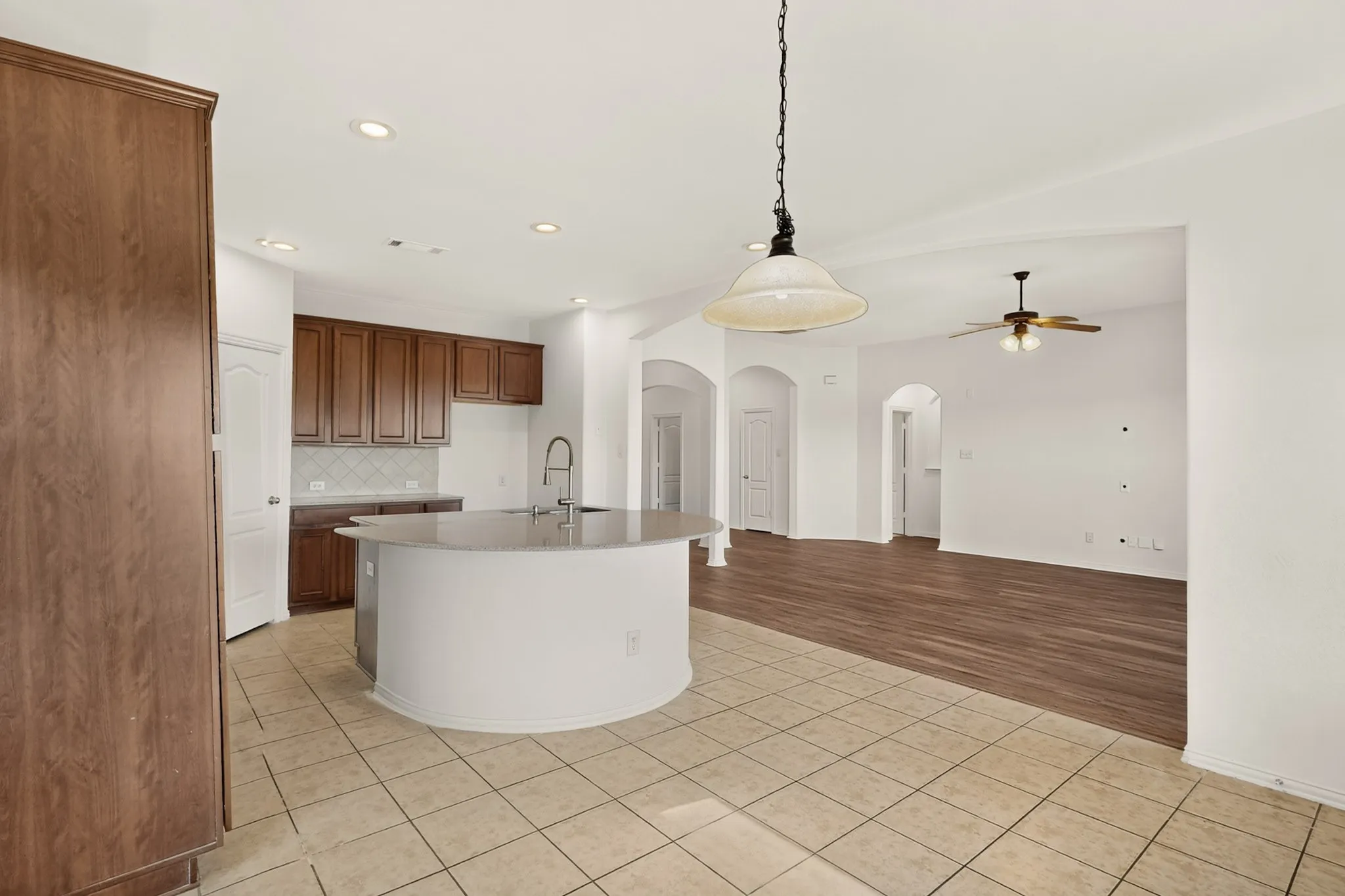 Kitchen featuring wood-finish cabinetry, tile flooring, recessed lighting, and a curved island with an undermount sink