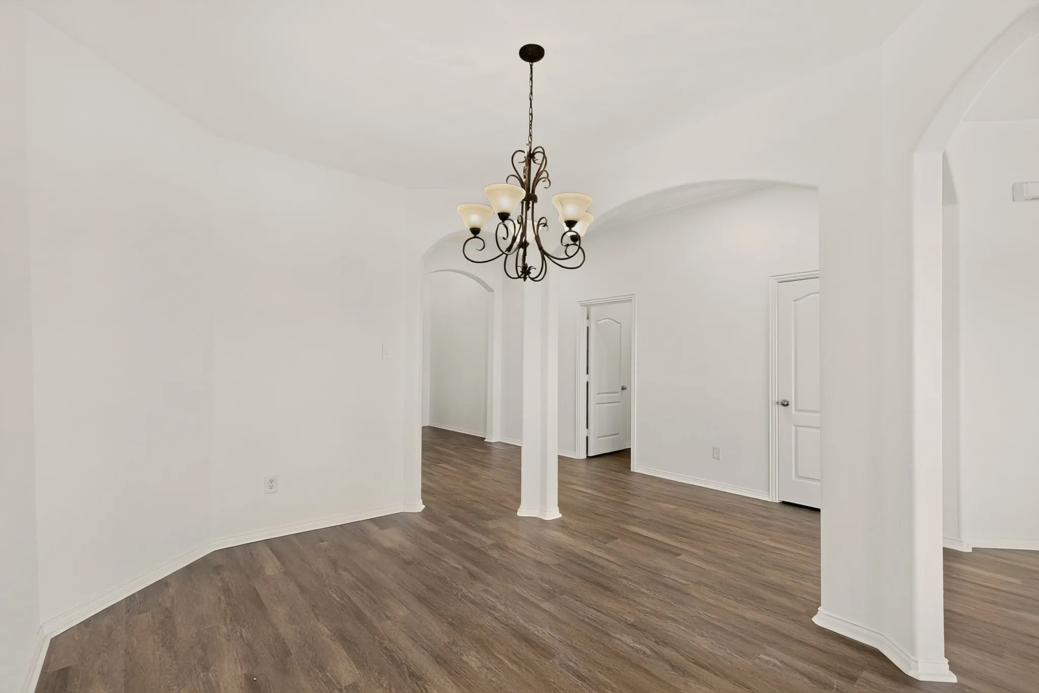 Wood-finish flooring, arched doorways, interior columns, and a decorative chandelier