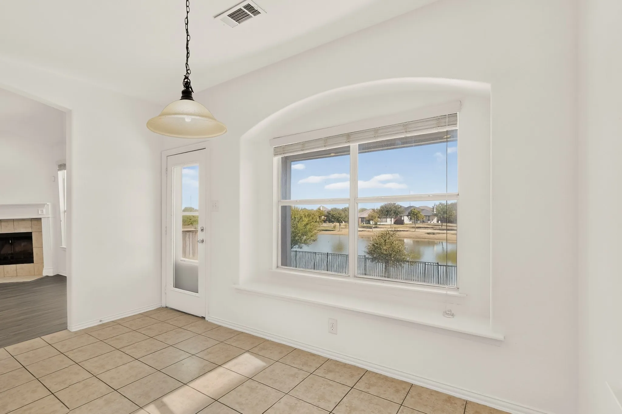 Arched window with water scenery, tile flooring, glass-paneled door, and a pendant light fixture