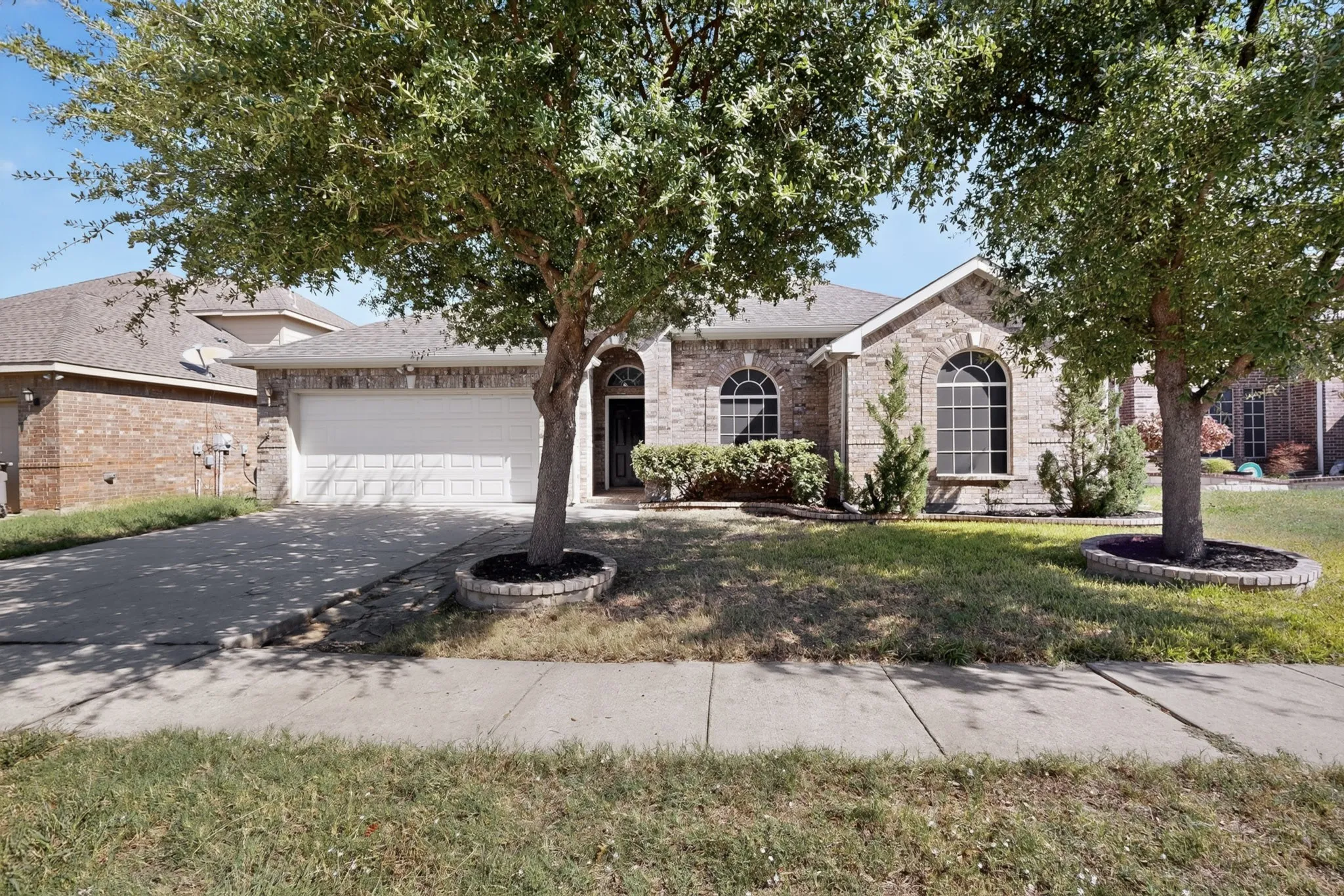 Brick veneer exterior with arched windows, an attached two-car garage, and mature trees