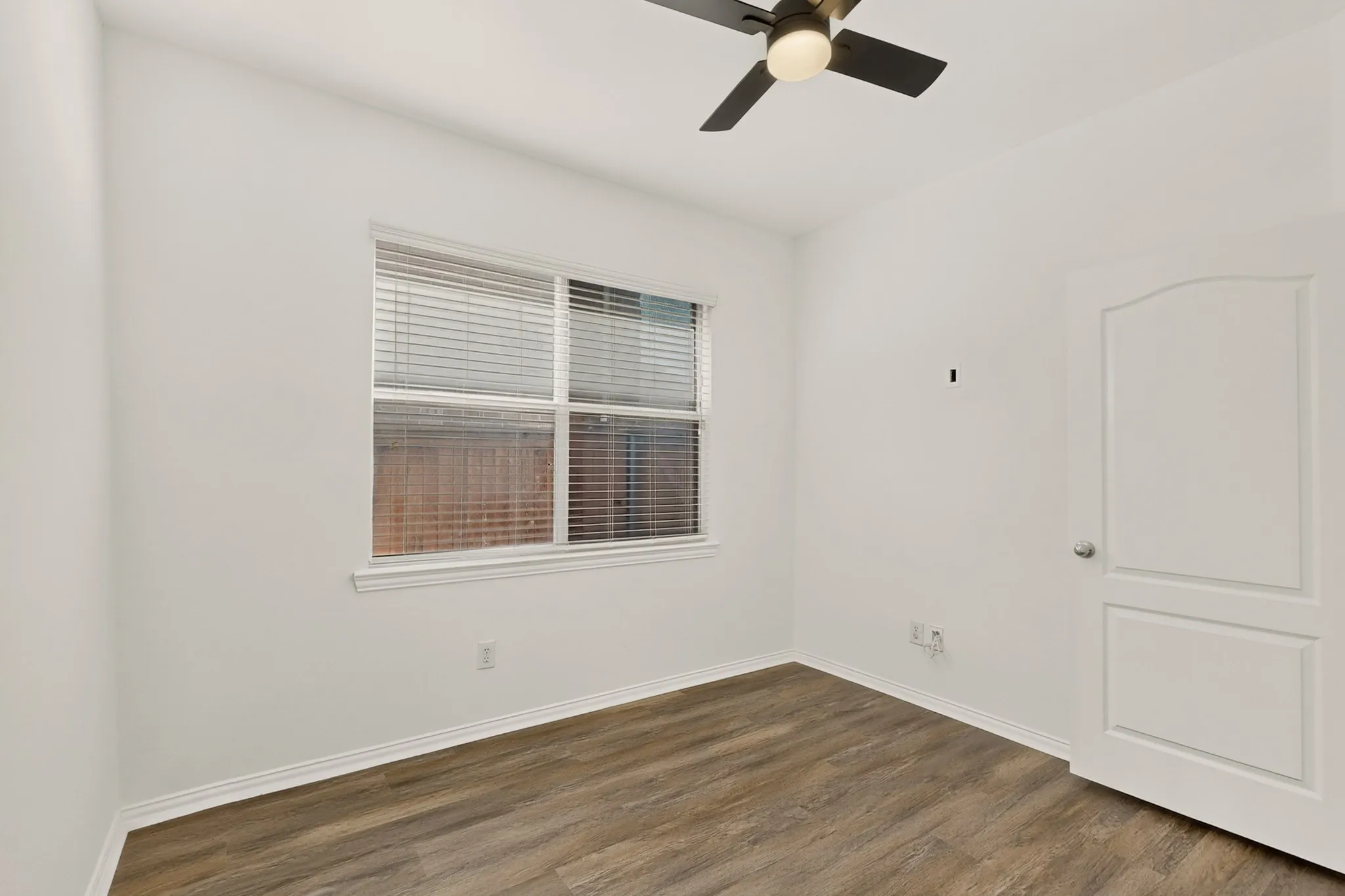 Wood-finish flooring, white walls, and a window with blinds