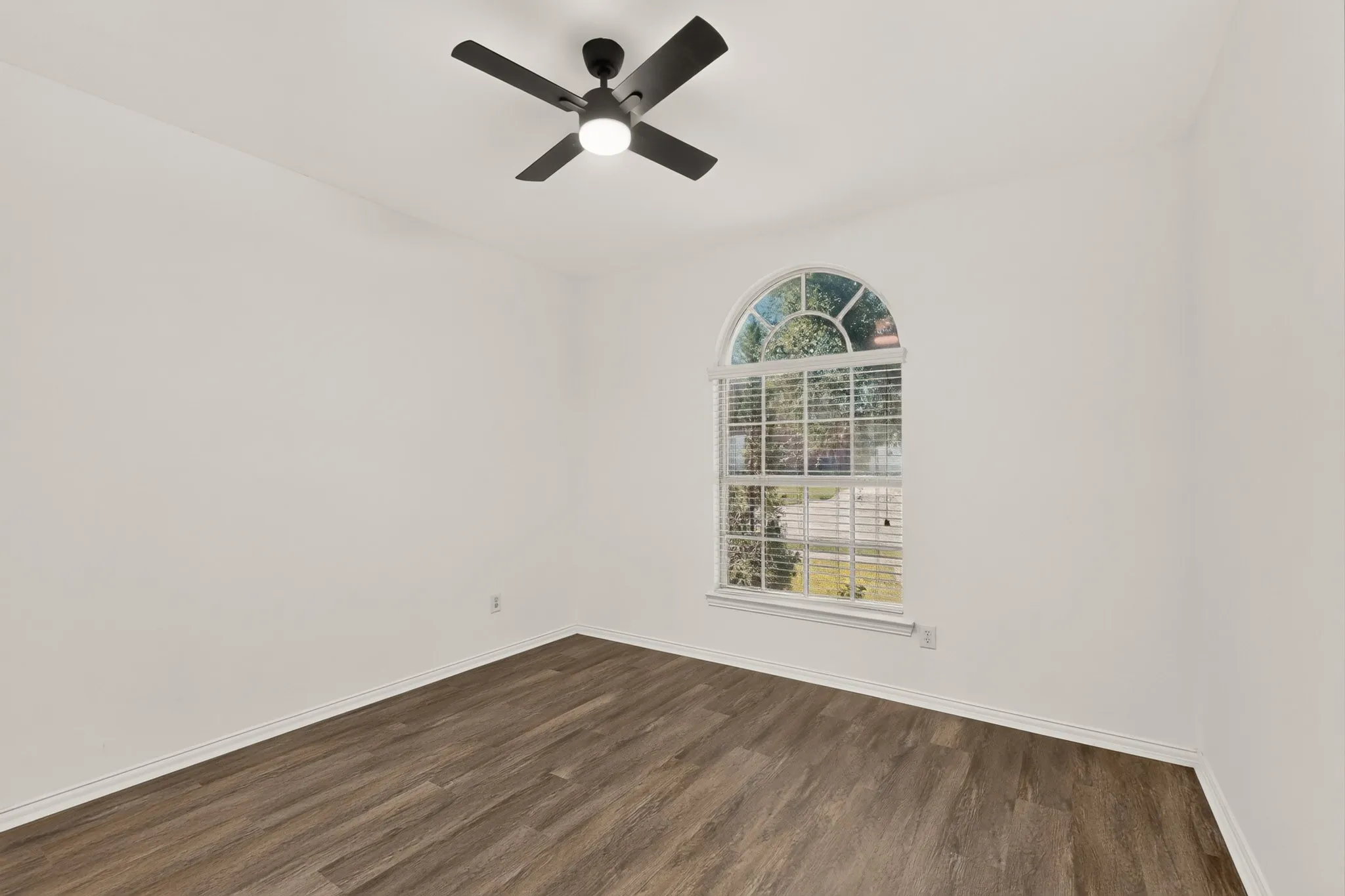 Arch-top window with blinds, wood-finish flooring, white walls, and a ceiling fan with integrated lighting