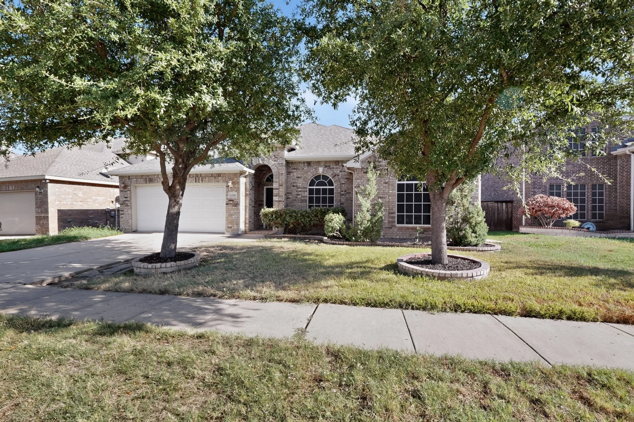 Brick exterior with arched entry, dual garage doors, arched windows, and mature trees