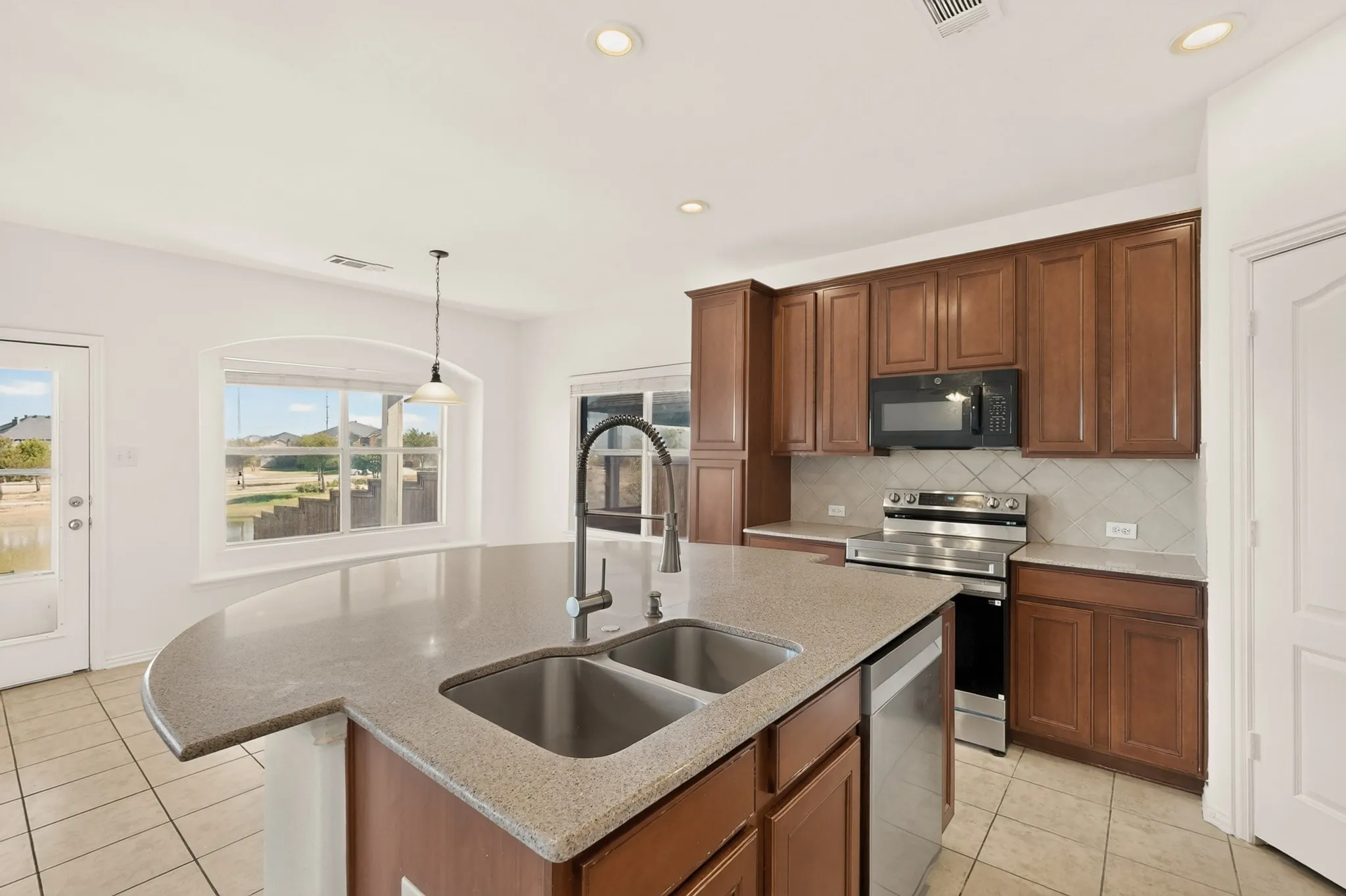 Kitchen featuring a curved island with integrated double sink, wood cabinetry, stainless steel appliances, and a tiled backsplash