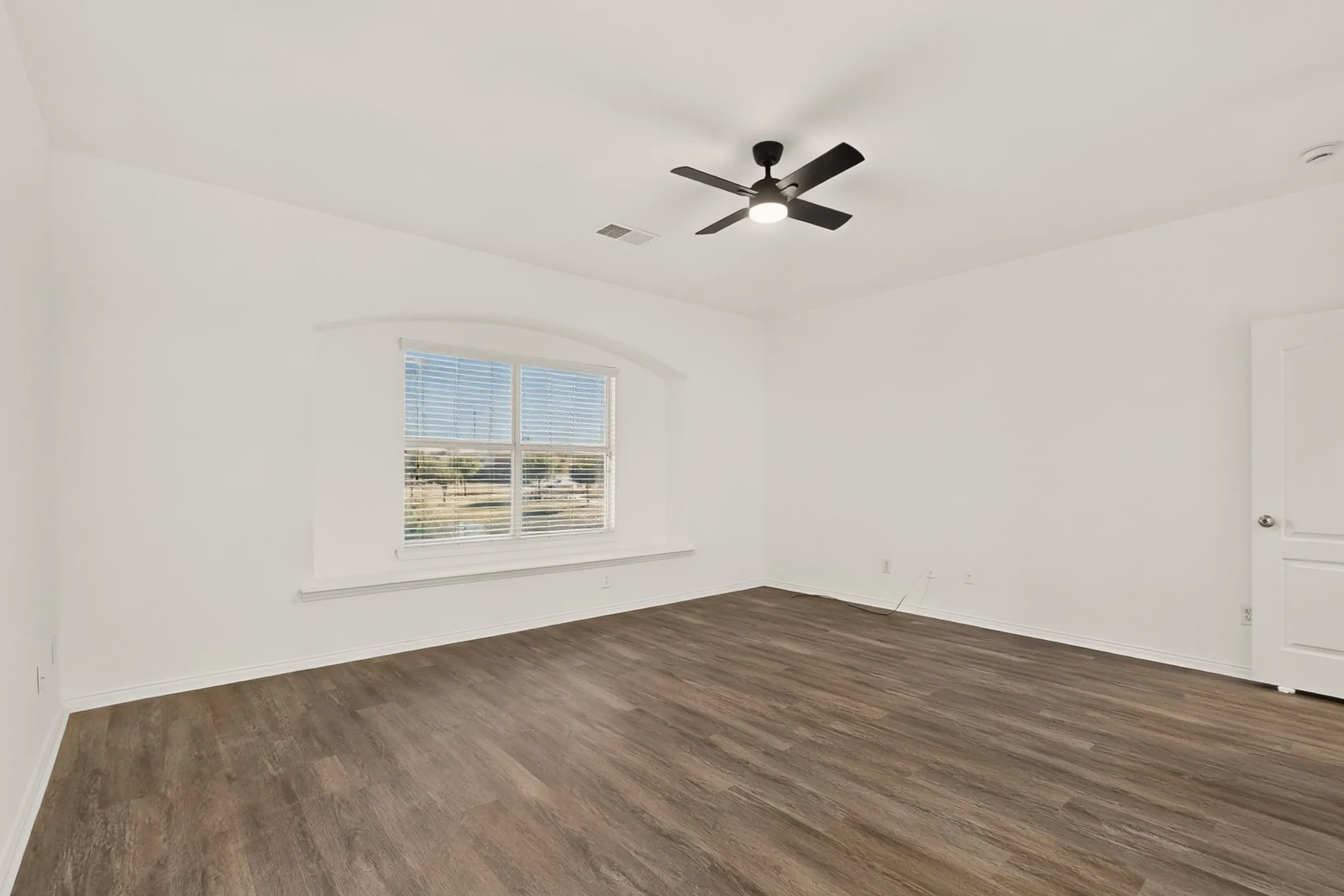 Wood-finish flooring, white walls, arched window, ceiling fan with integrated lighting, and a white panel door