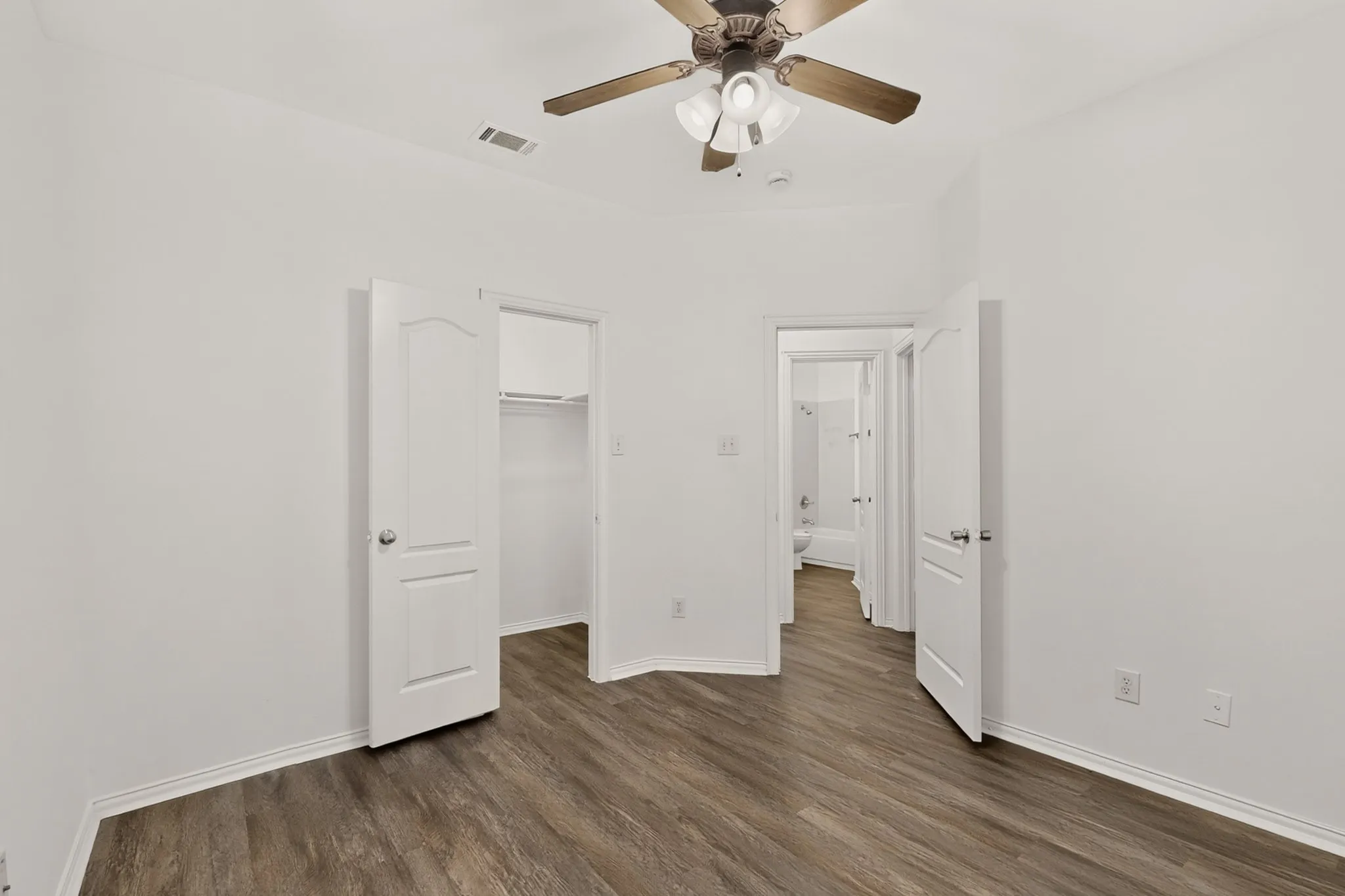 Wood-finish flooring with white baseboards, white walls, and a ceiling fan with integrated lighting