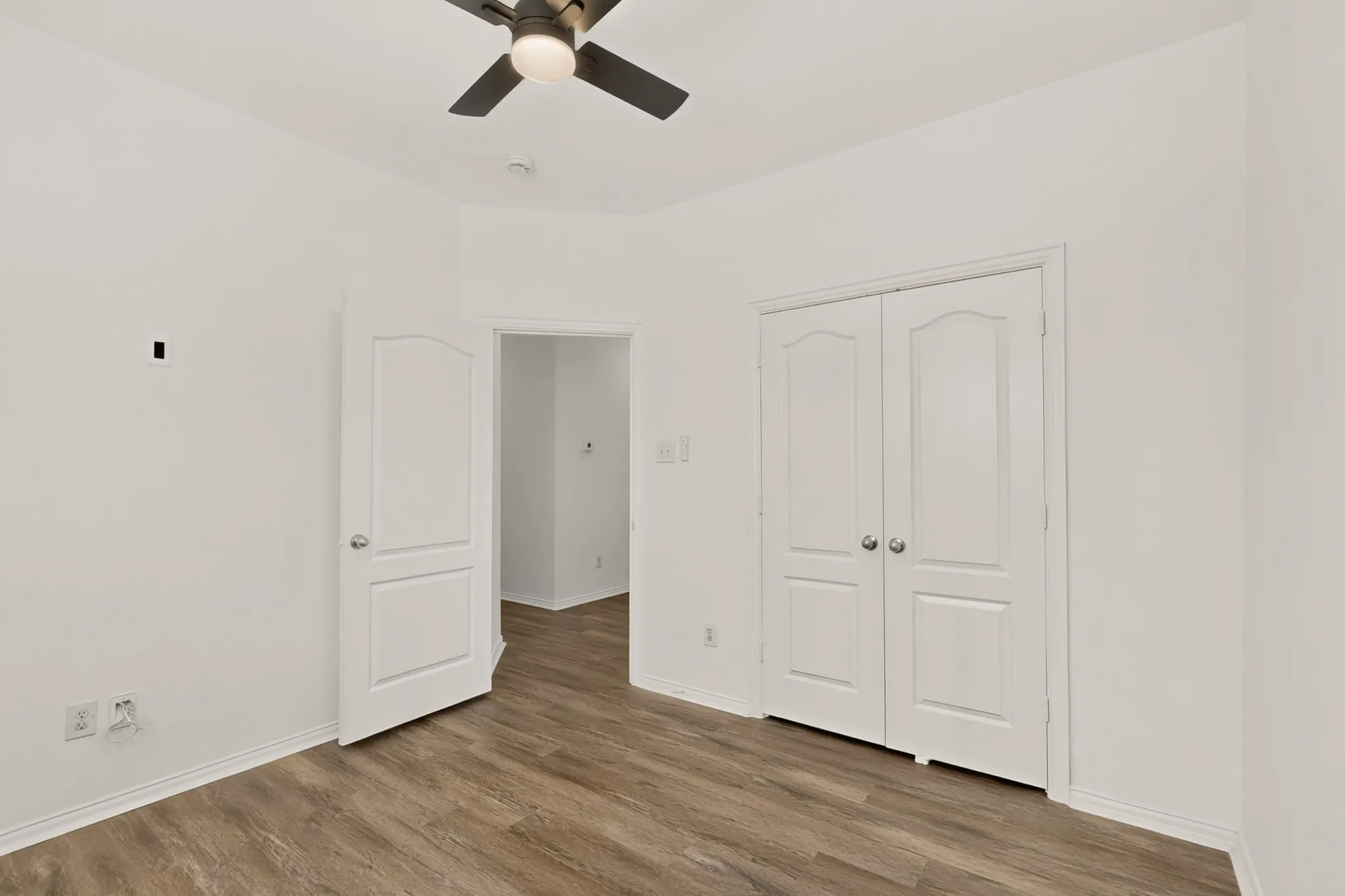 Wood-finish flooring, white paneled doors, ceiling fan with integrated lighting, and white walls