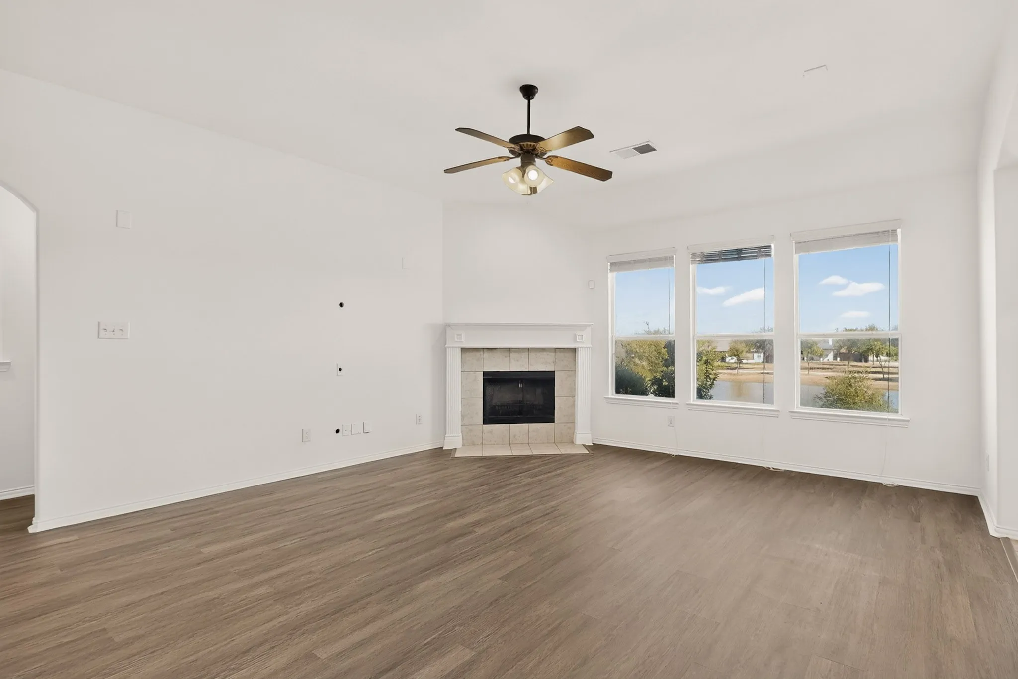 Spacious living area featuring wood-finish flooring, a ceiling fan with brushed metal finish, and a fireplace with stone surround