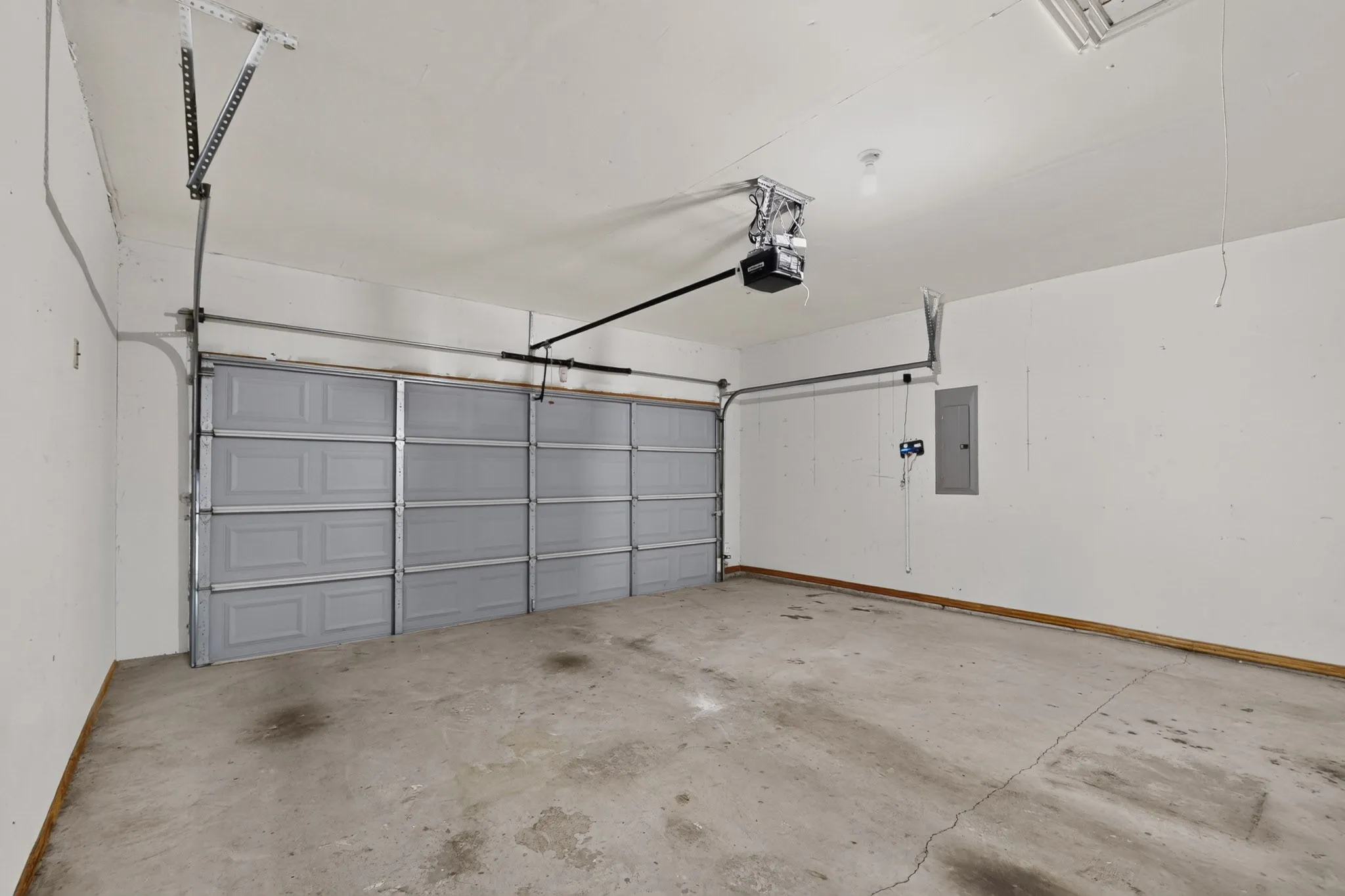 Attached garage with a gray sectional door, concrete flooring, and an overhead door opener