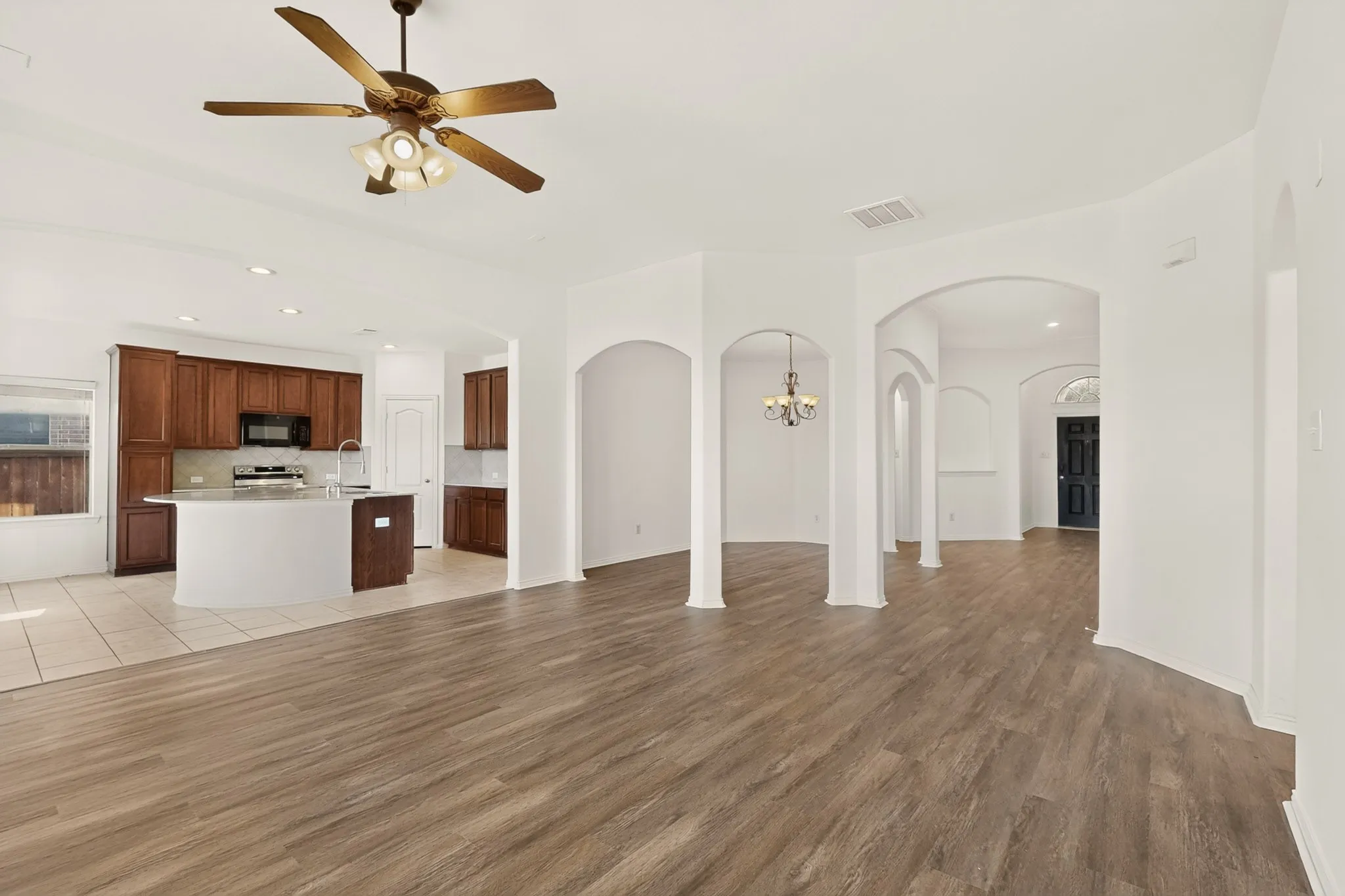 Open-concept living area with wood-finish flooring, recessed lighting, and architectural archways