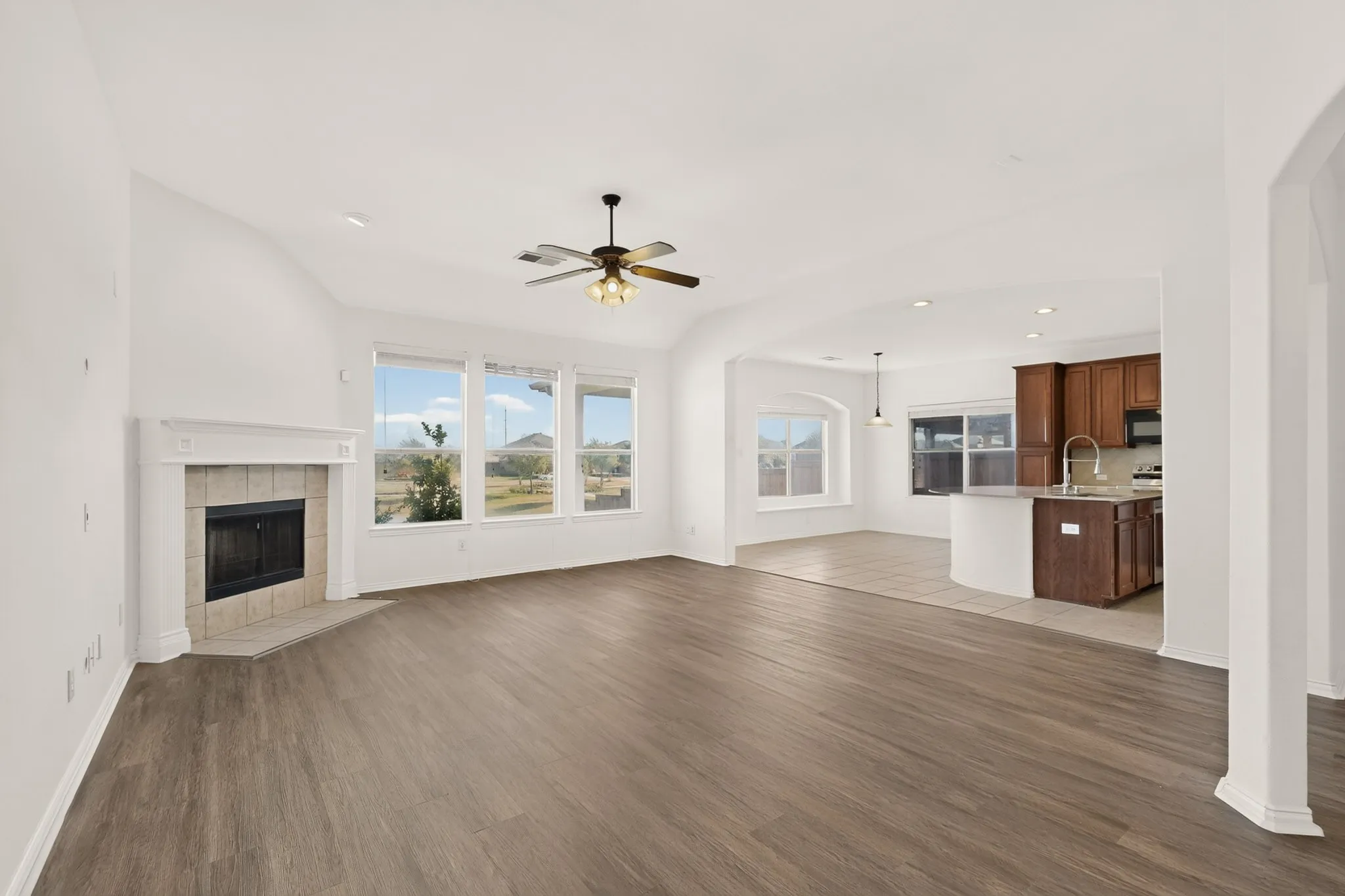 Spacious living area featuring wood-finish flooring, a corner fireplace with a tiled surround, and multiple large windows