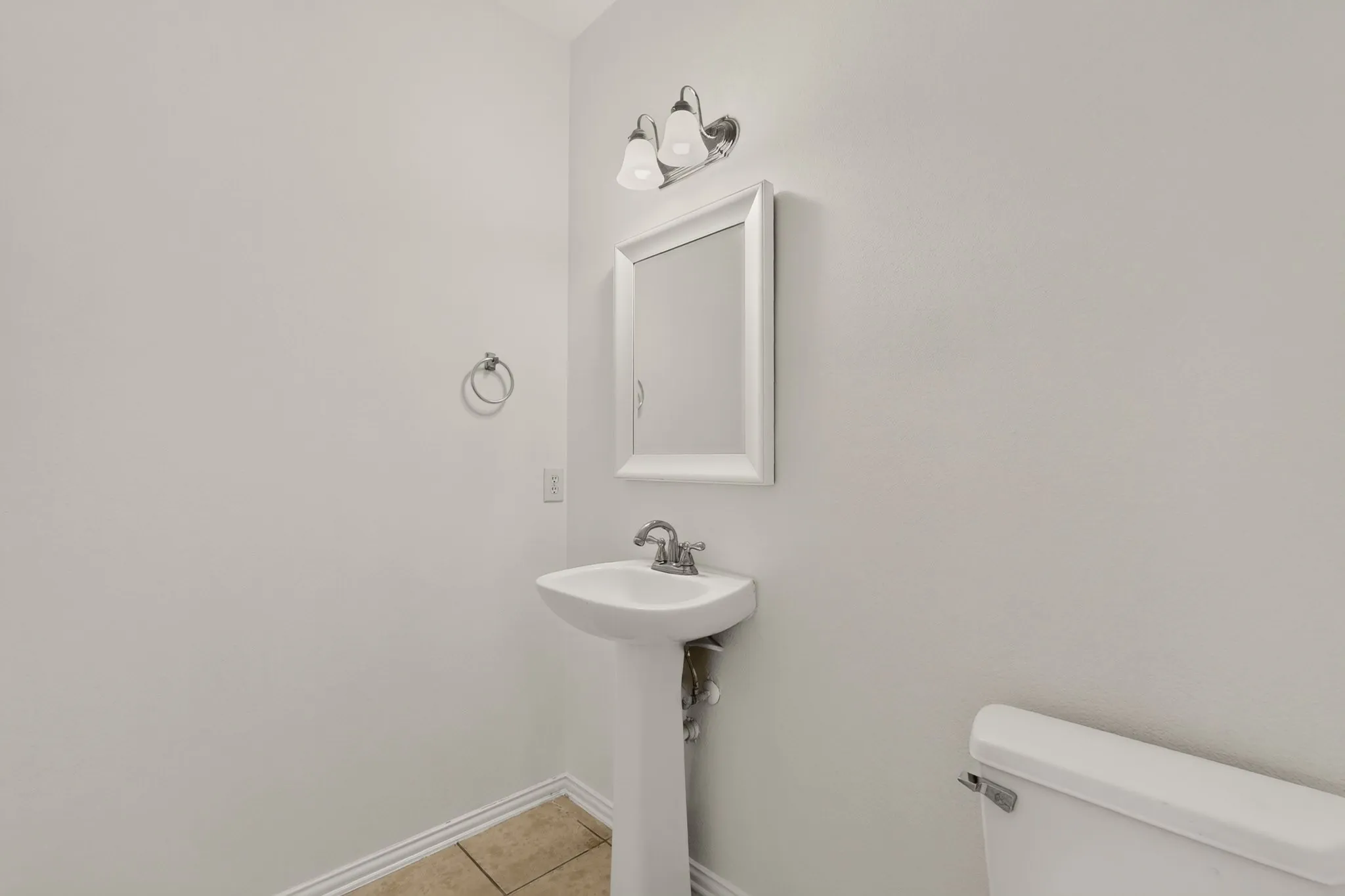 Pedestal sink, wall-mounted mirror, ceramic tile flooring, and wall-mounted vanity lighting