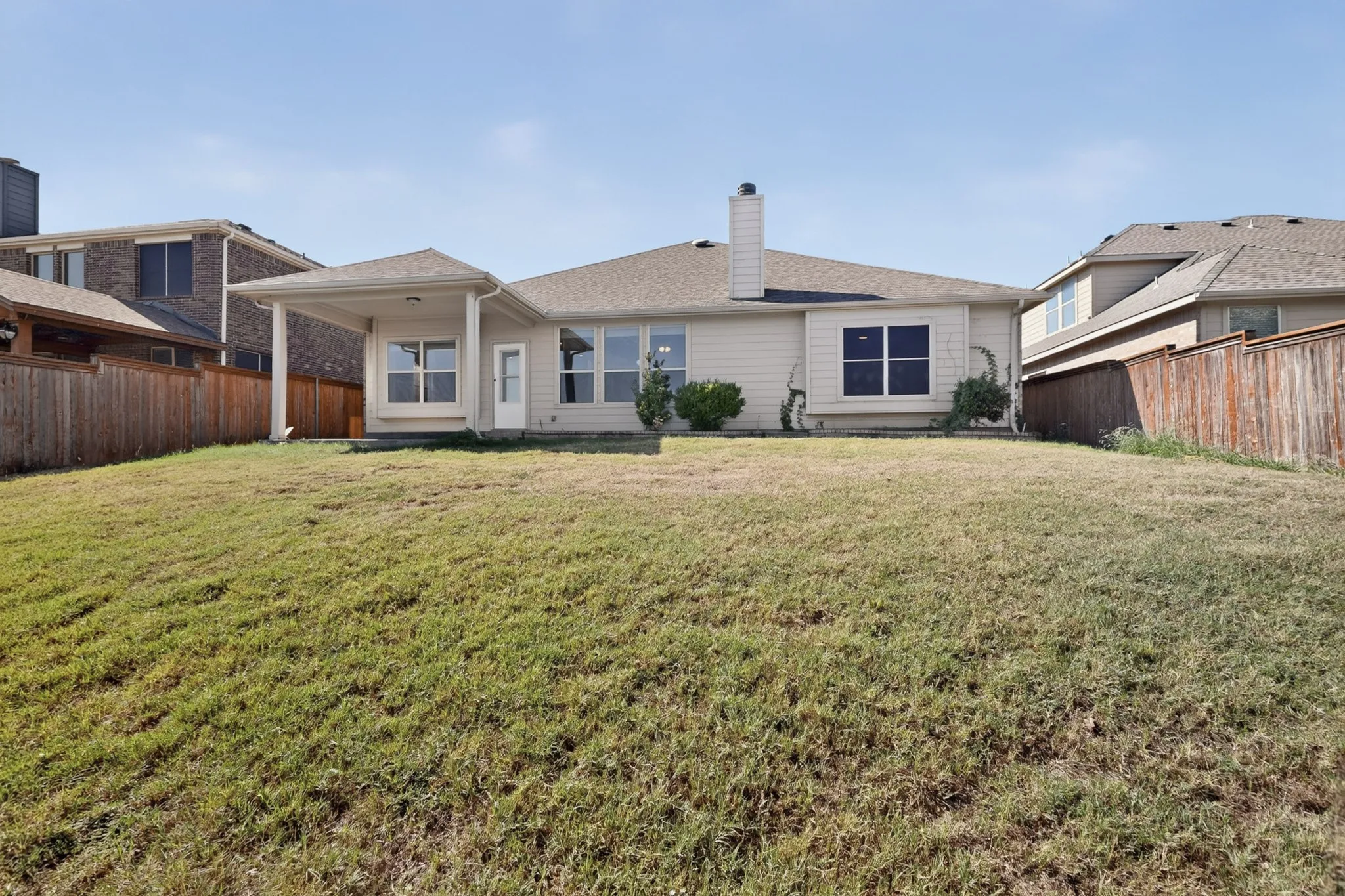 Charming single-story residence featuring a spacious rear lawn, professional landscaping with mature foundation plantings, and a clean architectural design with multiple windows allowing natural light throughout