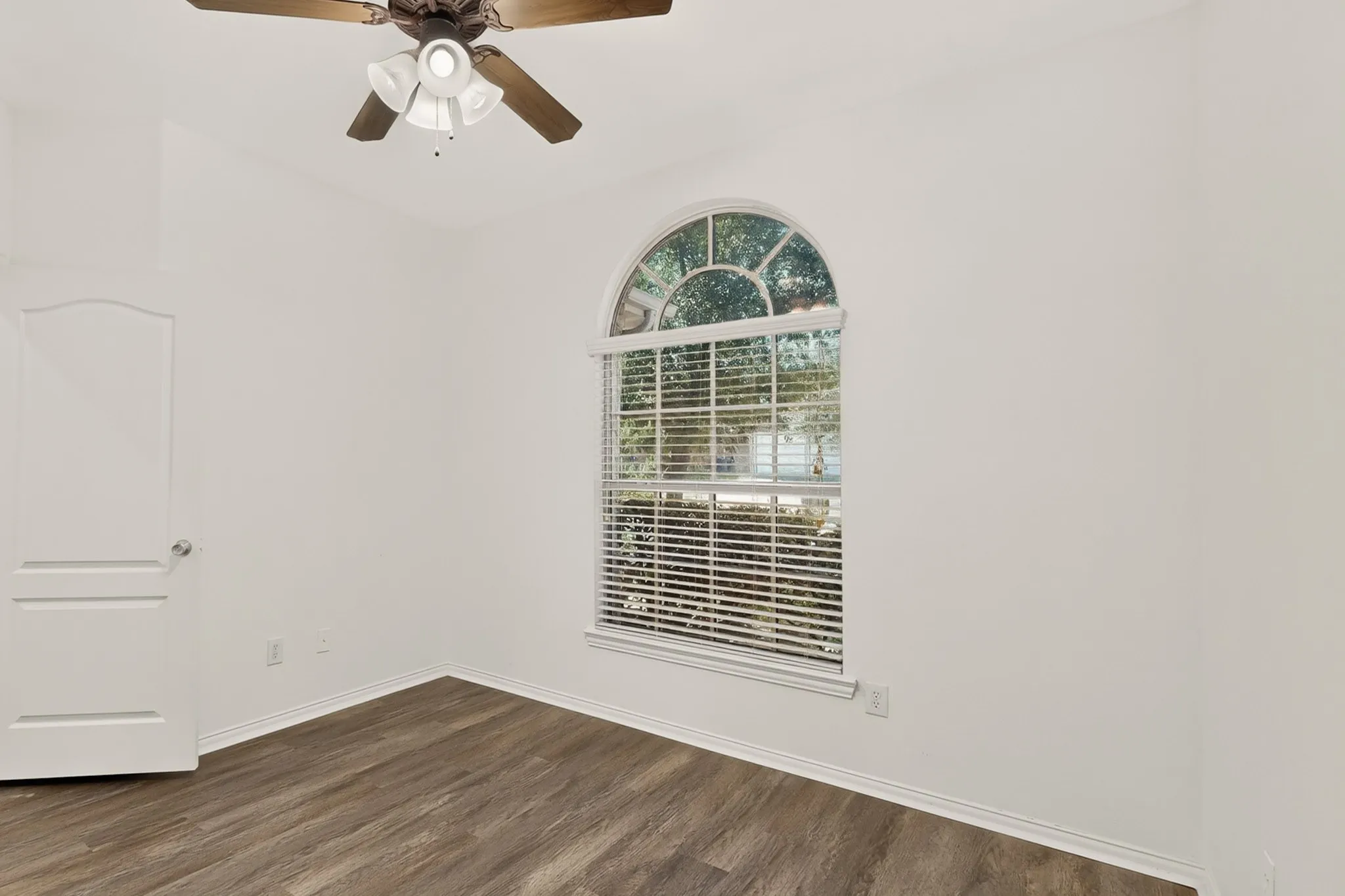 Arched window with blinds, wood-finish flooring, ceiling fan, and white interior paint