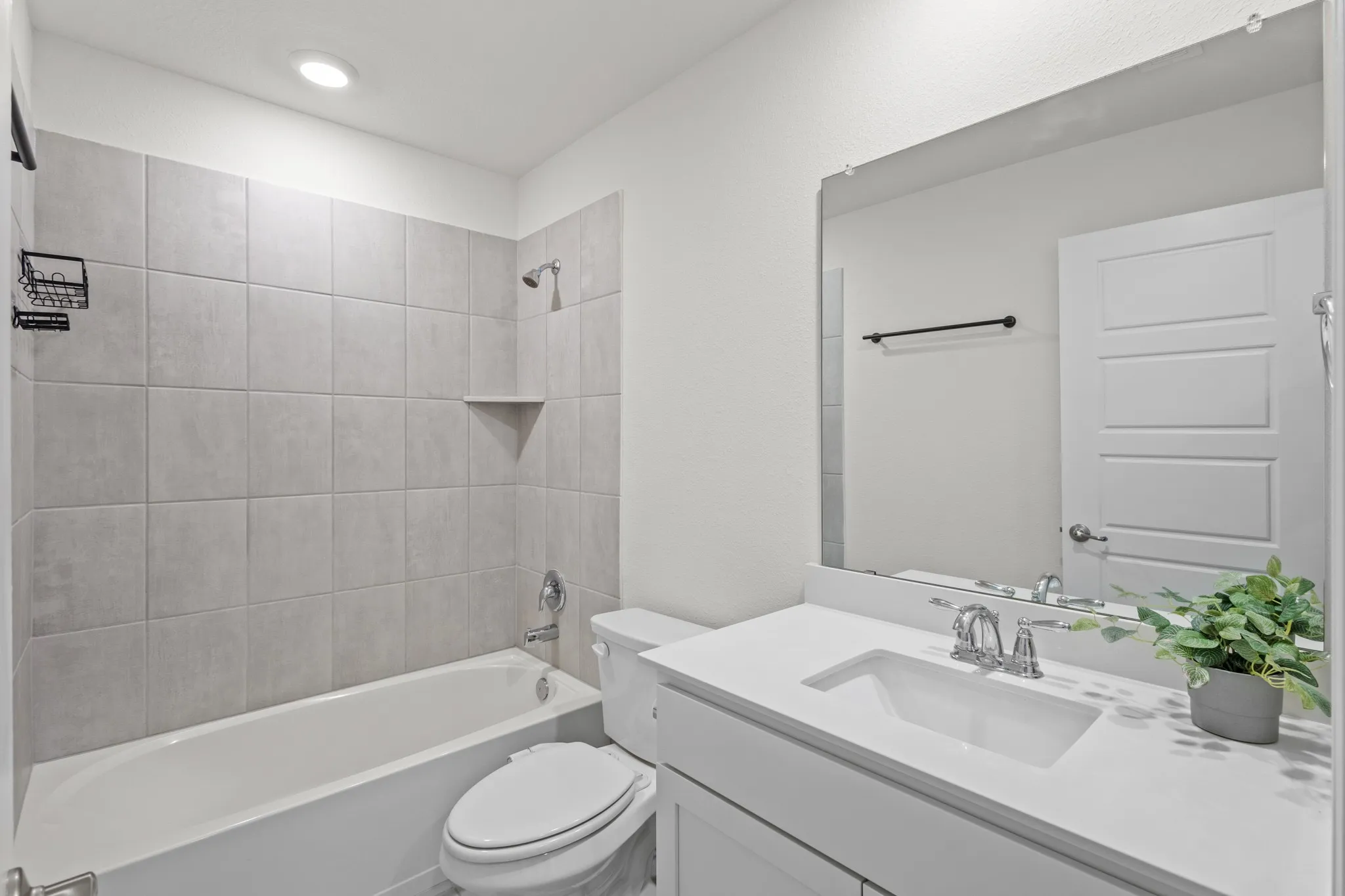 Built-in bathtub with light gray tile surround and recessed shelf