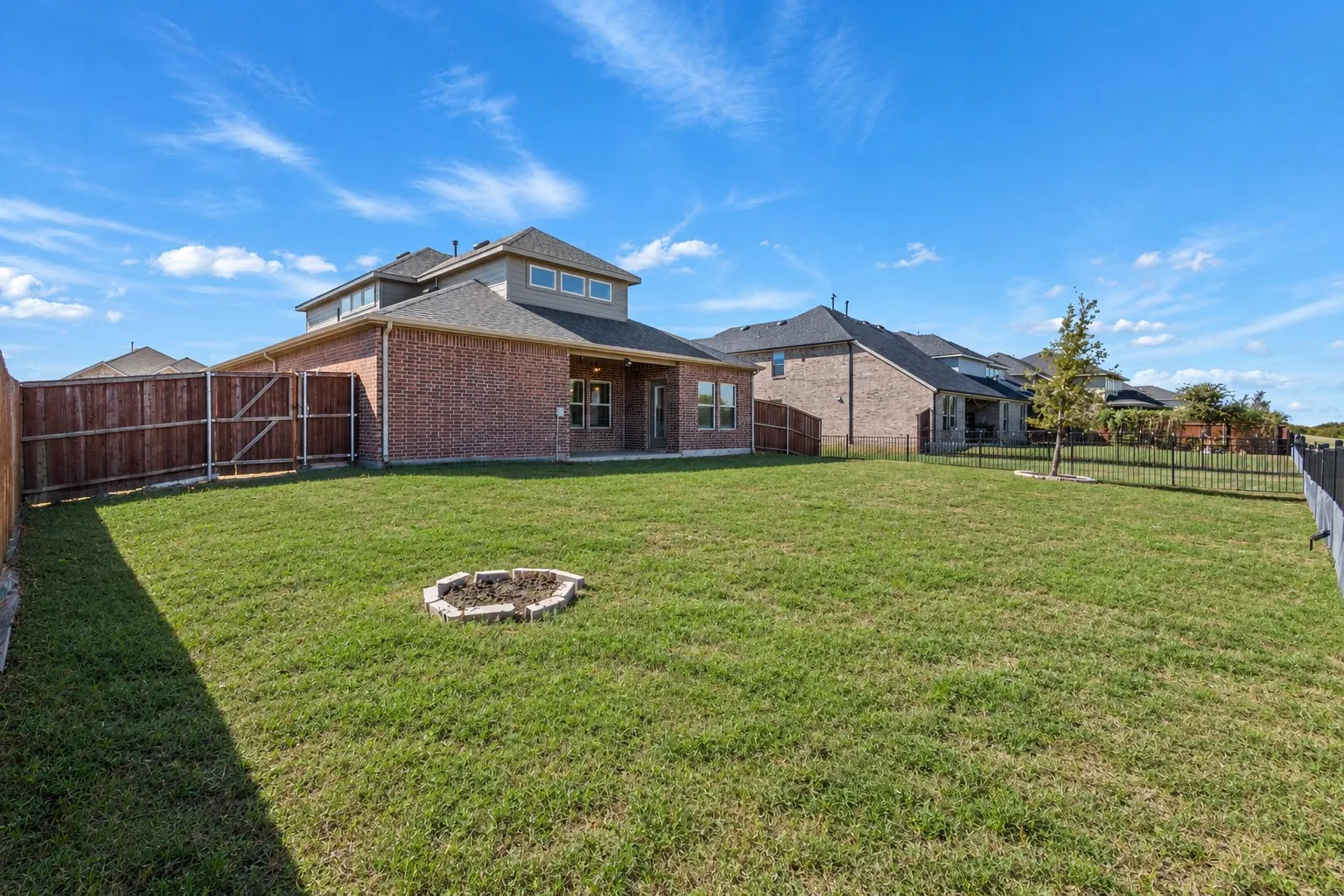 Expansive backyard featuring a manicured lawn, full privacy fencing, and a built-in fire pit