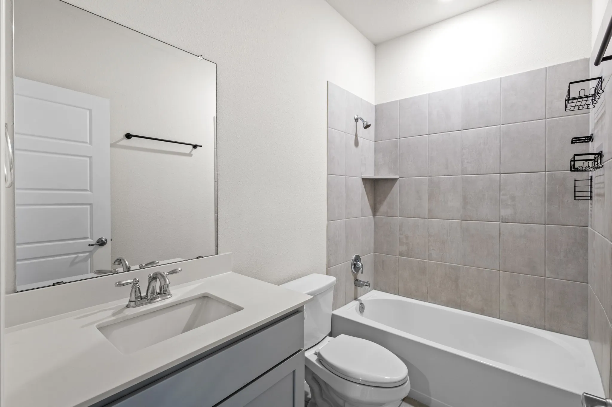 Bathroom featuring a single vanity with an undermount sink, a large wall-mounted mirror, a toilet, and a combination shower and tub with tile surround