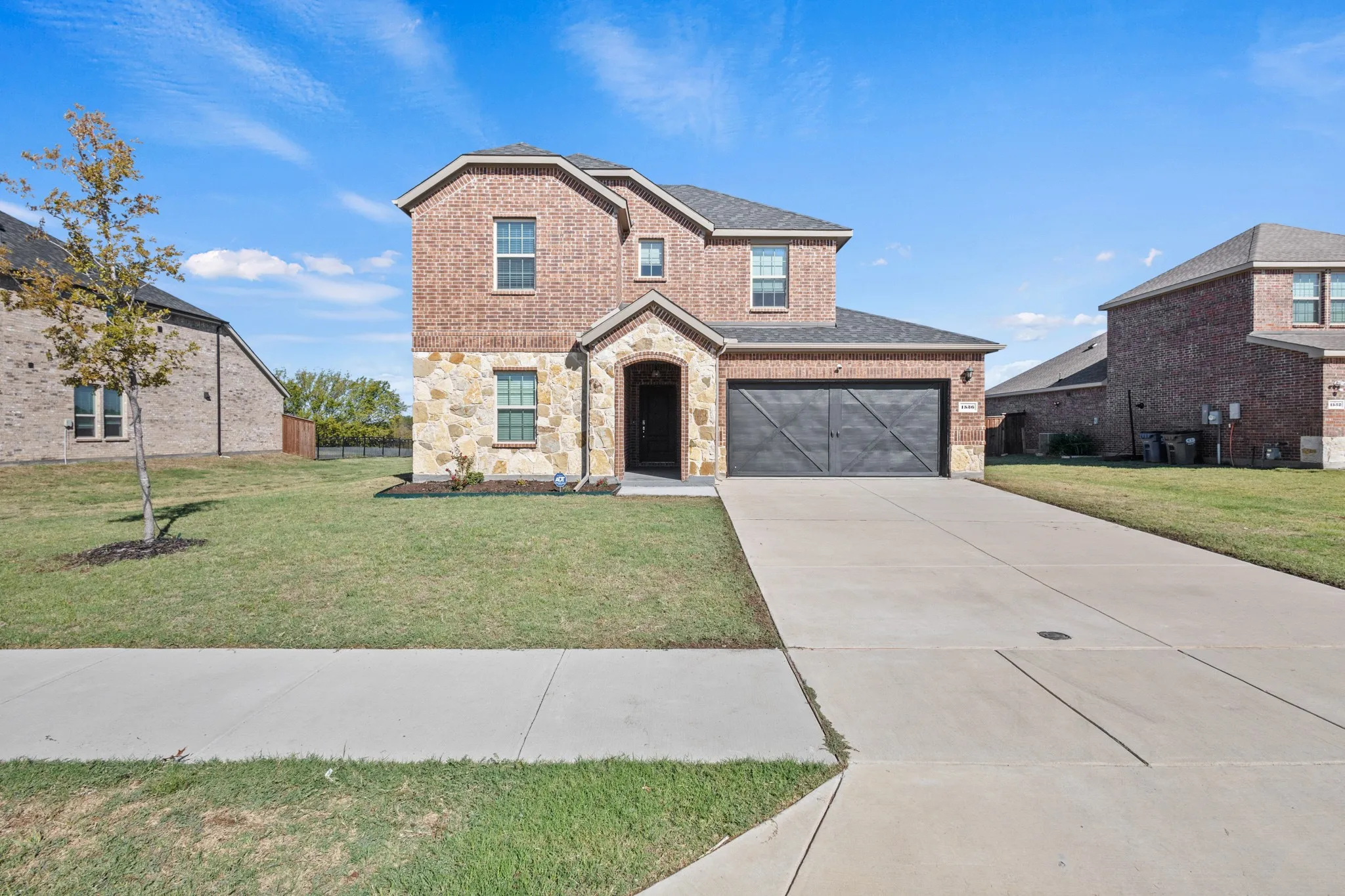 Brick and stone facade, arched entry, two-story construction, attached garage with decorative door, concrete driveway
