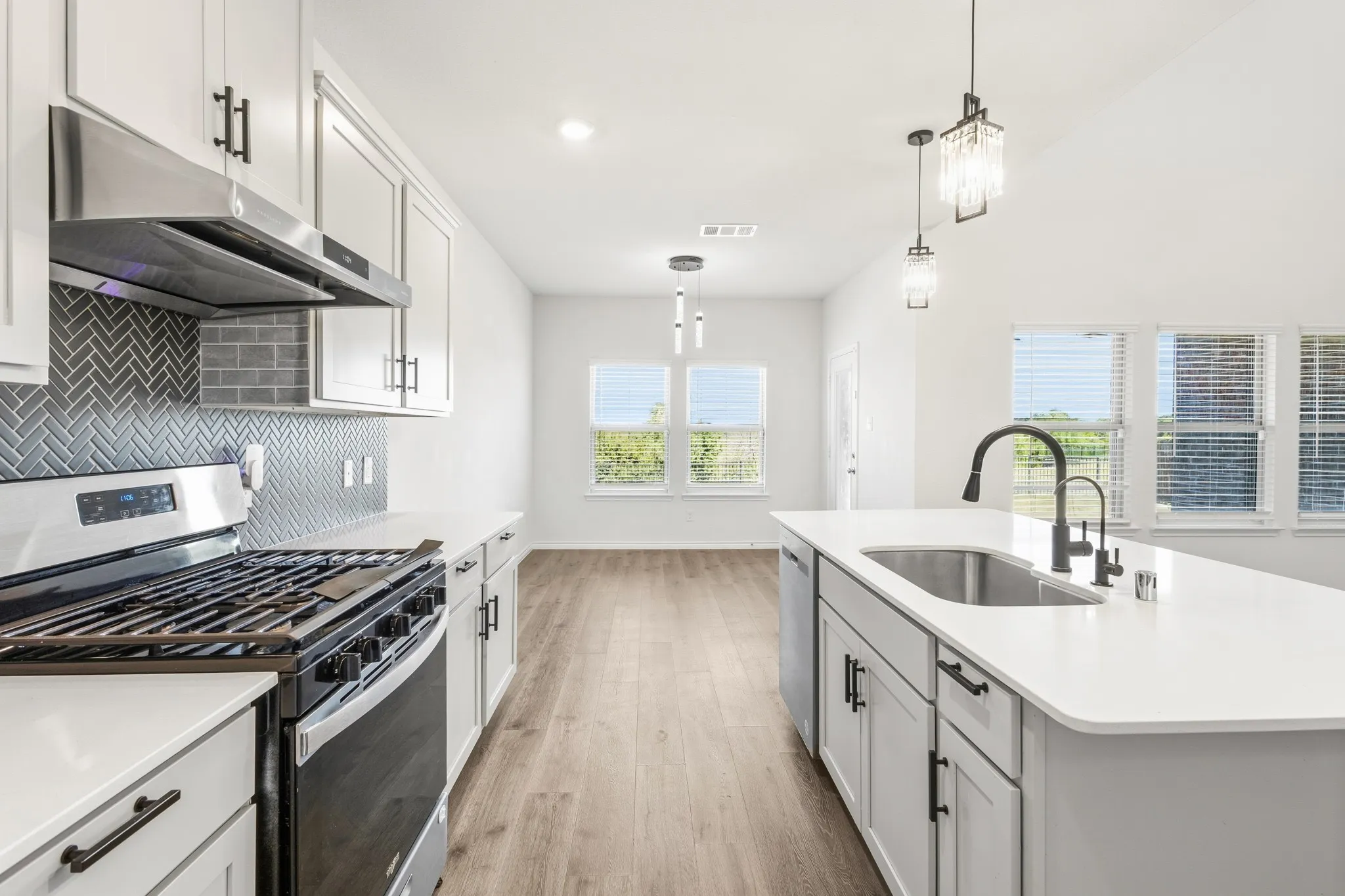 Modern kitchen featuring white cabinetry, a herringbone tile backsplash, stainless steel appliances, and an island with an undermount sink