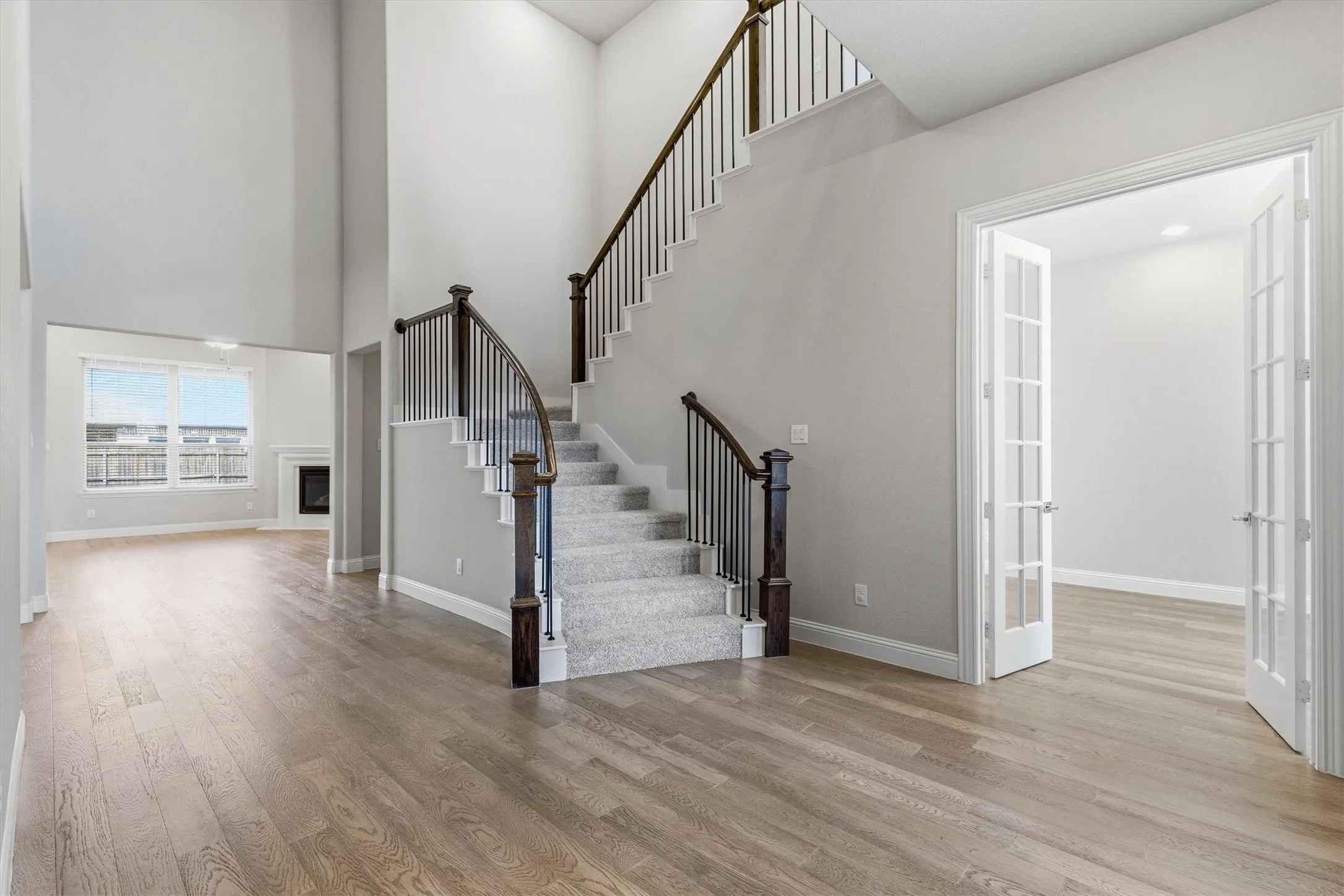 Two-story foyer with wood-finish flooring, a carpeted staircase with dark wood newel posts and metal balusters, and a room with French doors