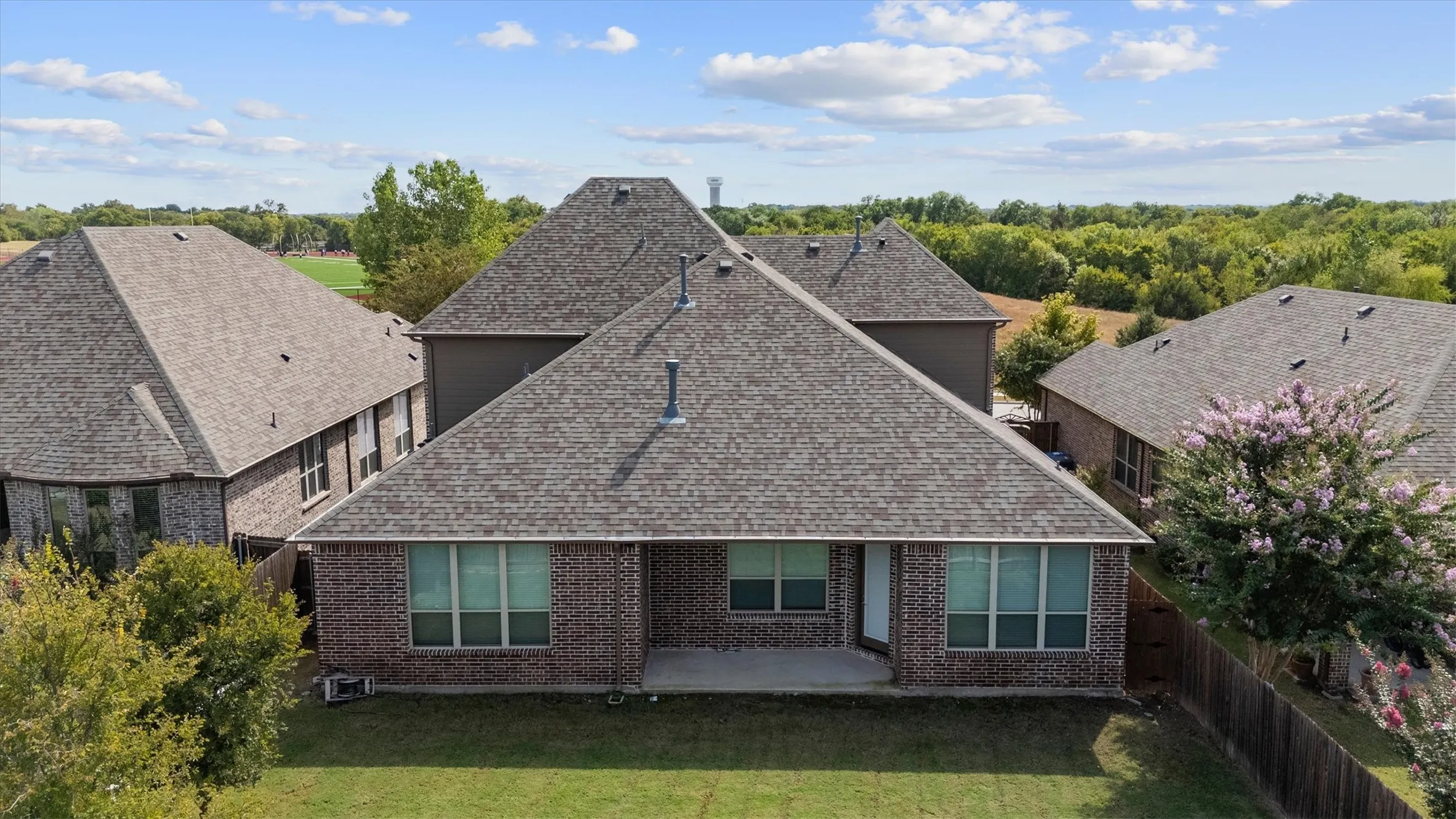 Rear exterior featuring a brick facade, covered patio, and a fenced yard with mature trees