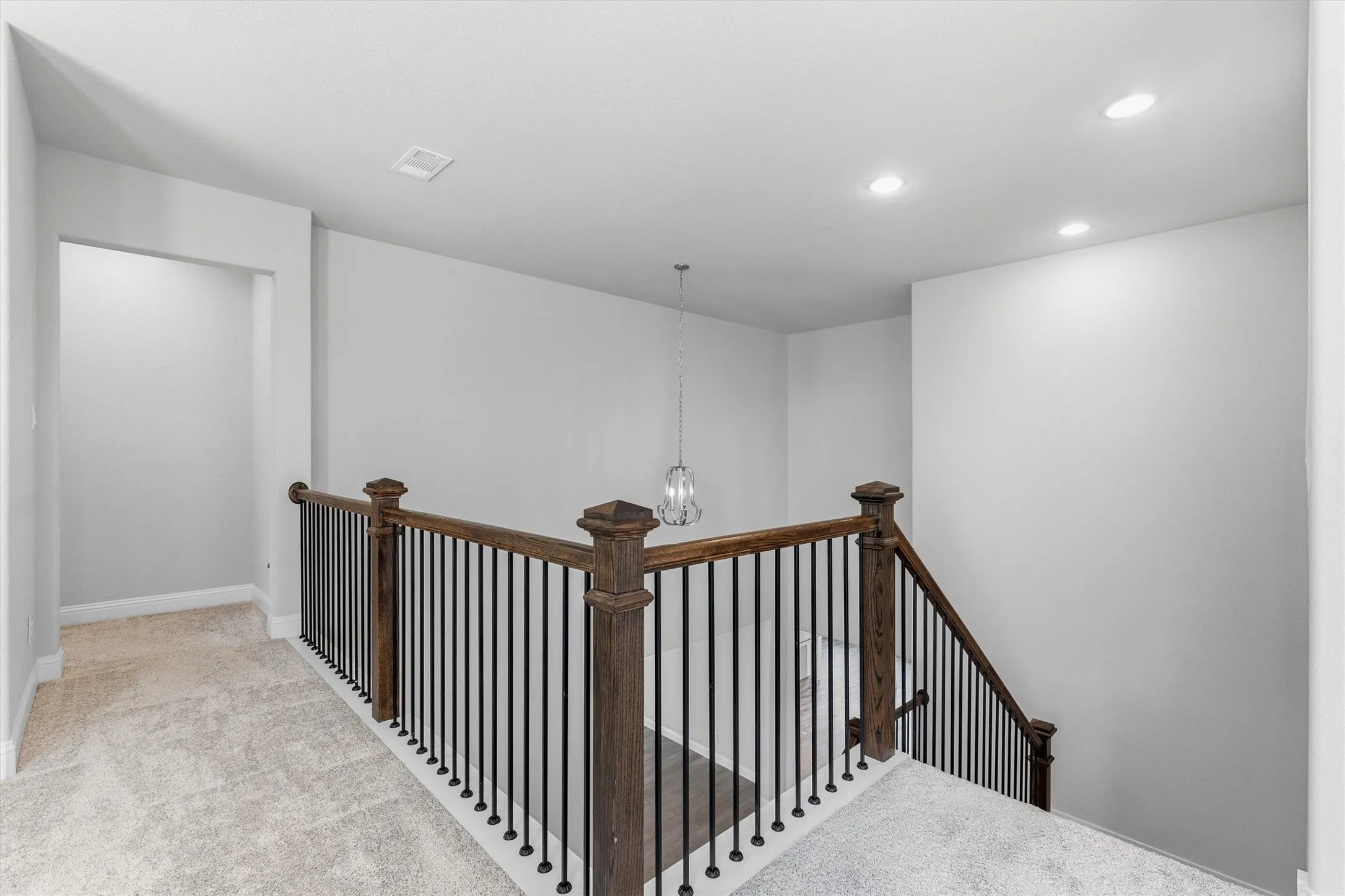Carpeted landing featuring recessed lighting, a decorative chandelier, and a wood and iron staircase railing
