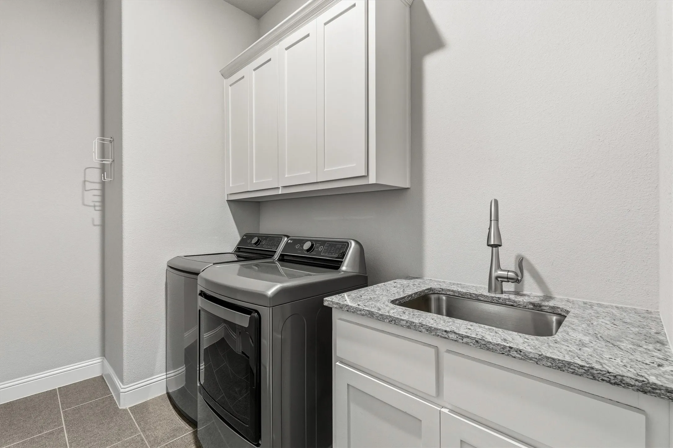 White upper cabinetry, solid surface countertop, stainless steel sink, and tile flooring