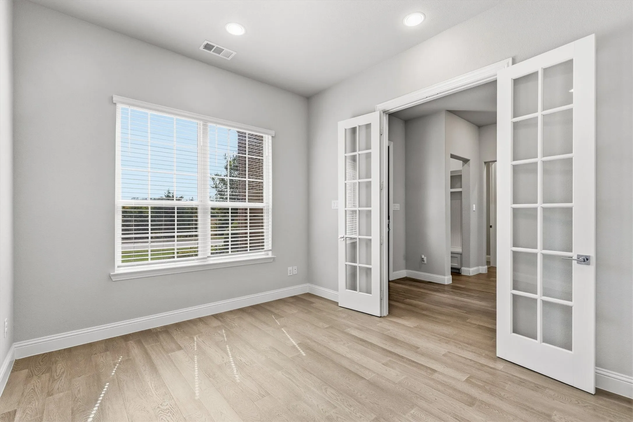 Light wood-finish flooring with recessed lighting and French doors