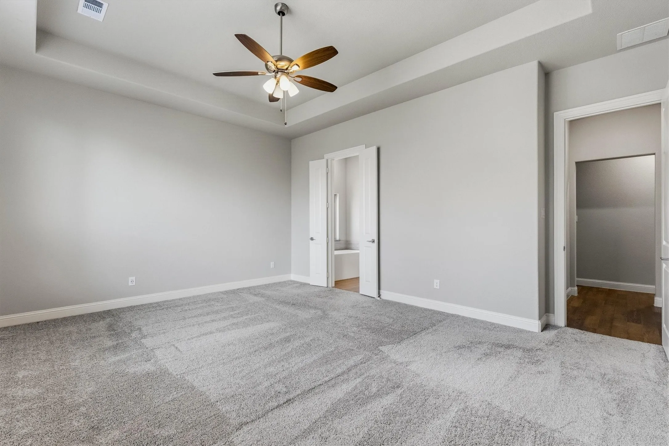 Spacious room with tray ceiling, ceiling fan, neutral gray walls, and light gray carpet