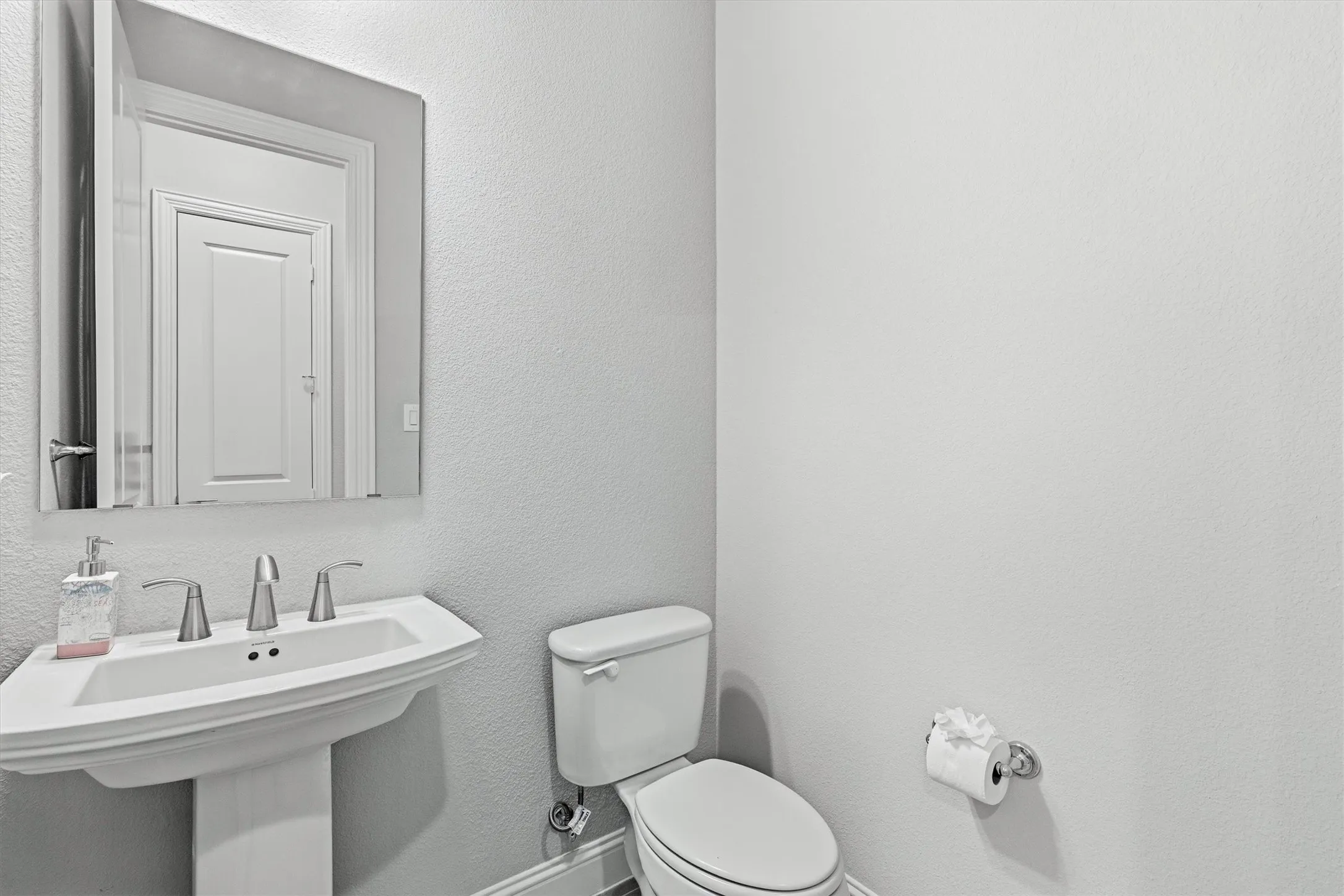 Pedestal sink with a polished chrome faucet, rectangular wall-mounted mirror, and a white toilet
